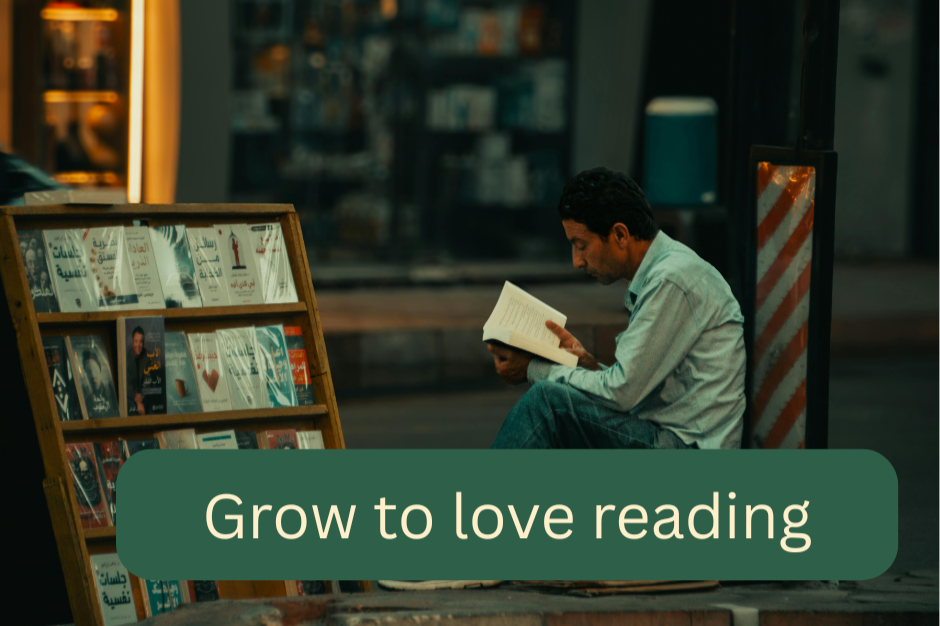 A man reading a book while sitting on the sidewalk outside a bookstore at night, with a sign that says 'Grow to love reading'.