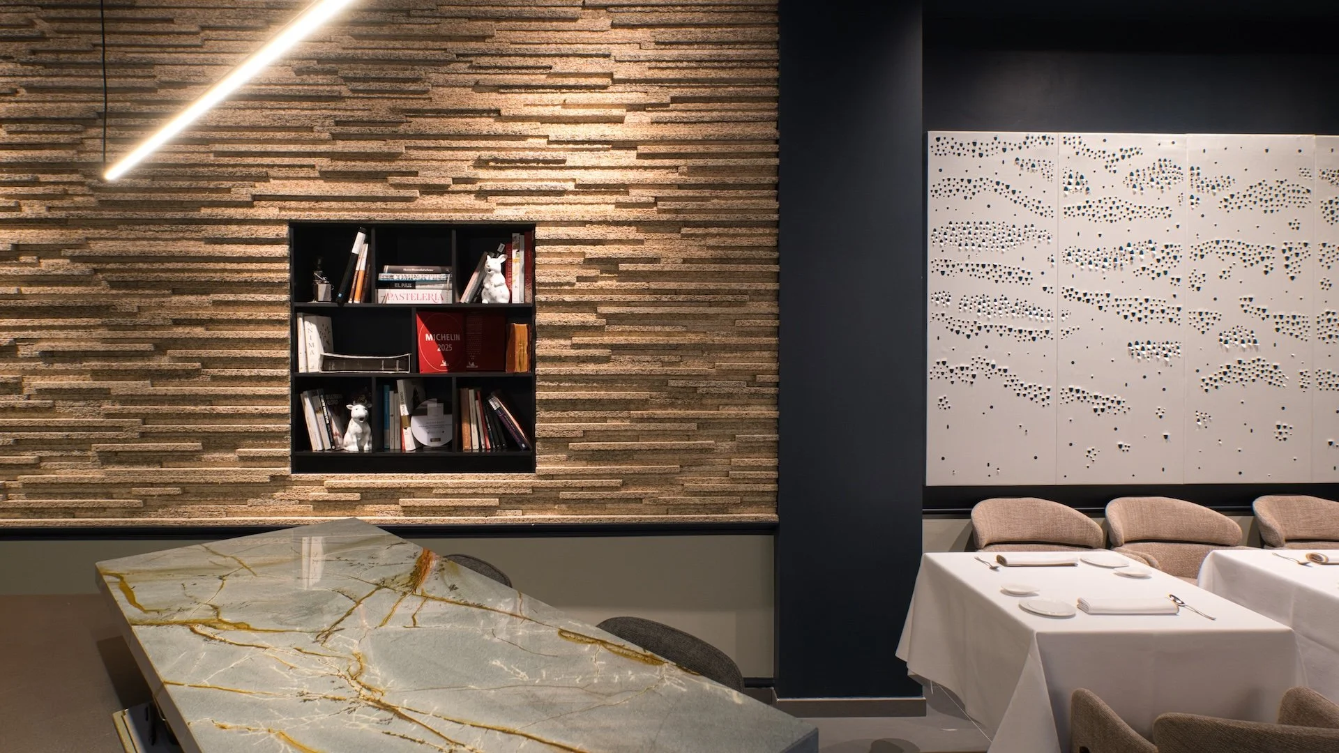 interior de restaurante con mesa de mármol, sillas tapizadas y paredes decoradas con ladrillos y paneles perforados