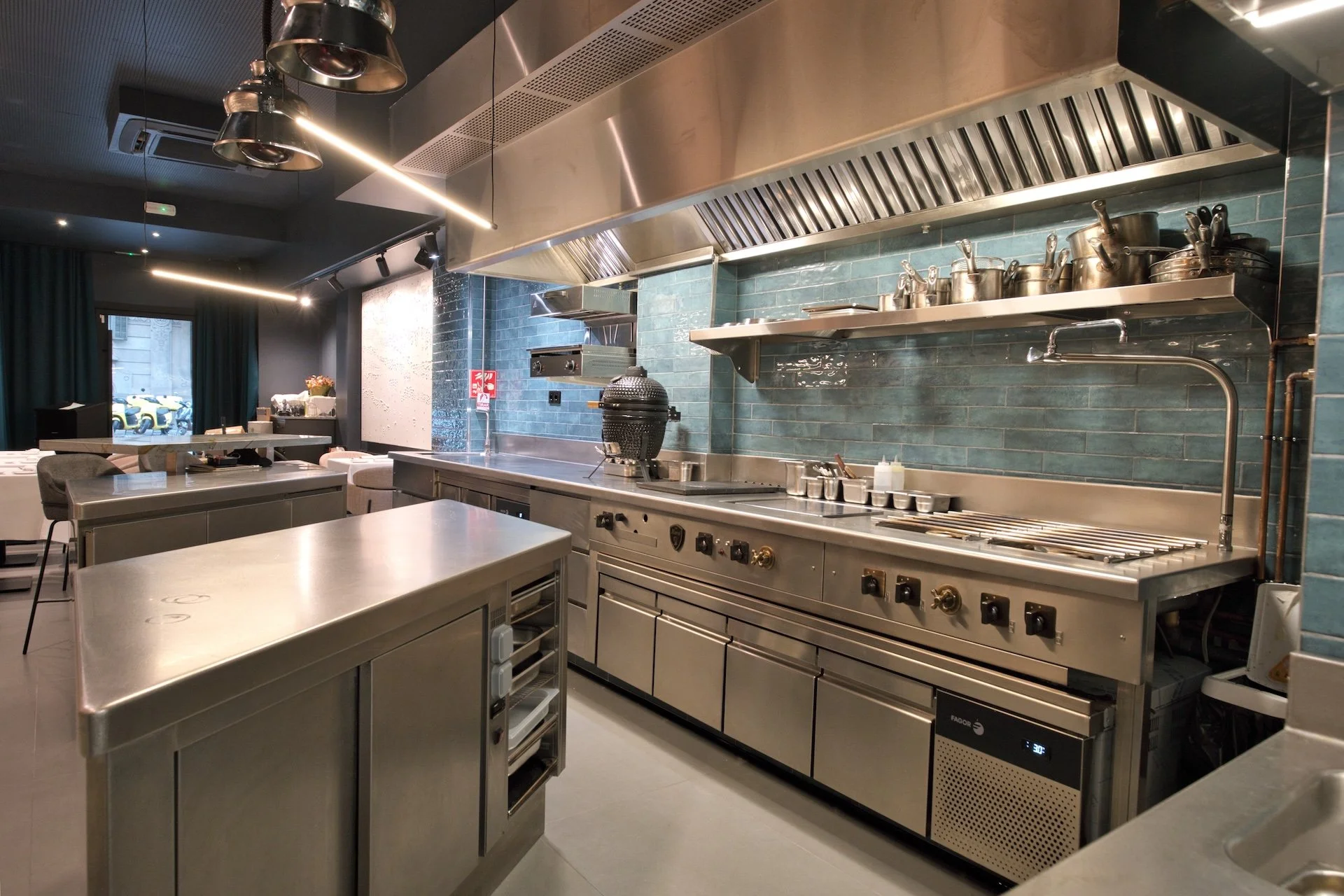 Cocina de restaurante moderna con encimera de acero inoxidable, utensilios, y paredes de azulejos azules.