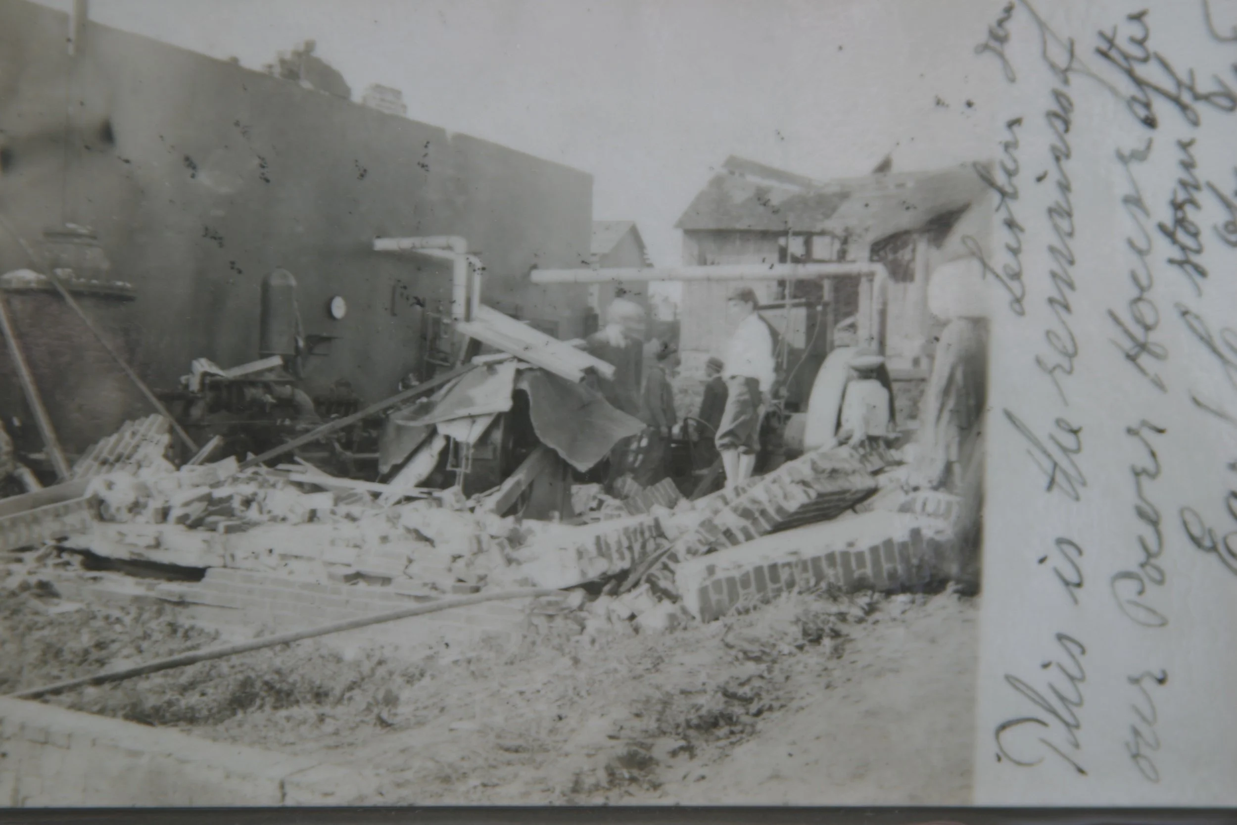 Black and white photograph of a construction site with workers standing around debris, construction machinery, and partially built structures, with handwritten notes on the right side.