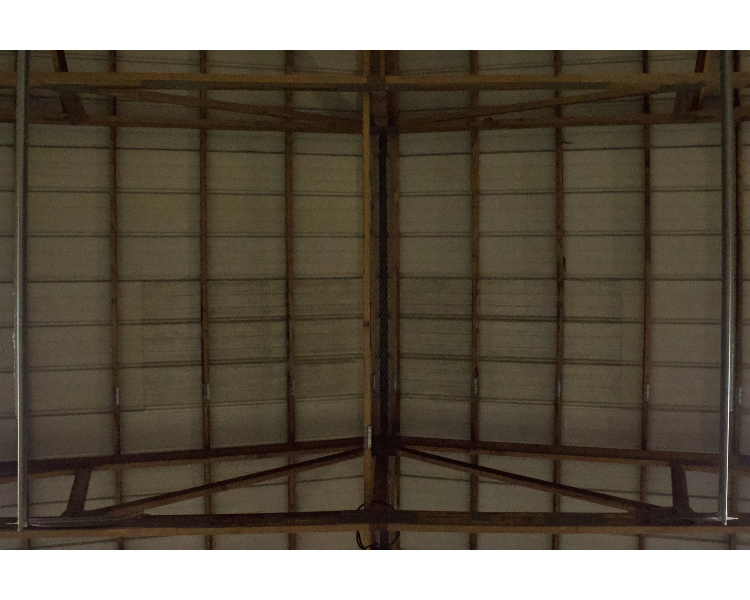 A view of the ceiling of an industrial or warehouse building showing wooden beams and metal supports.
