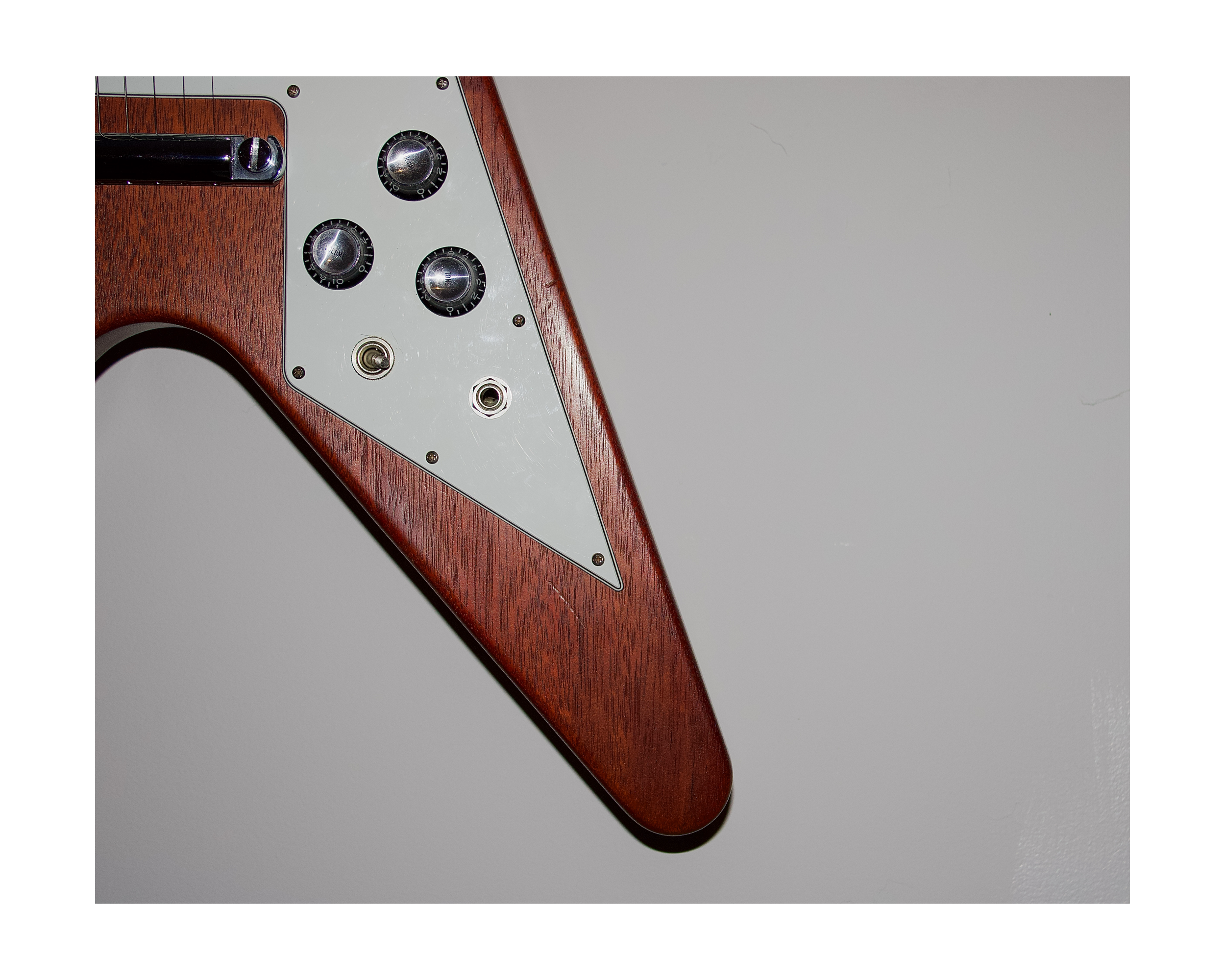 Close-up of a vintage electric guitar body with control knobs and switch, featuring a wooden neck and white pickguard, against a plain background.
