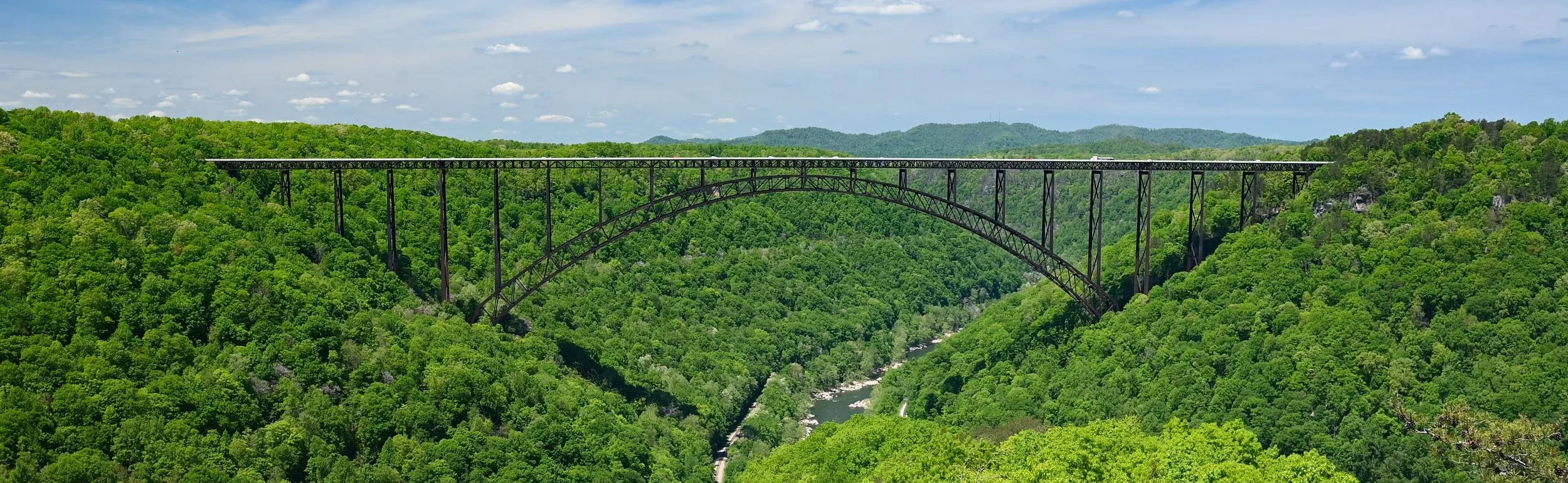 A trestle-style bridge spanning a valley and hills covered in green trees