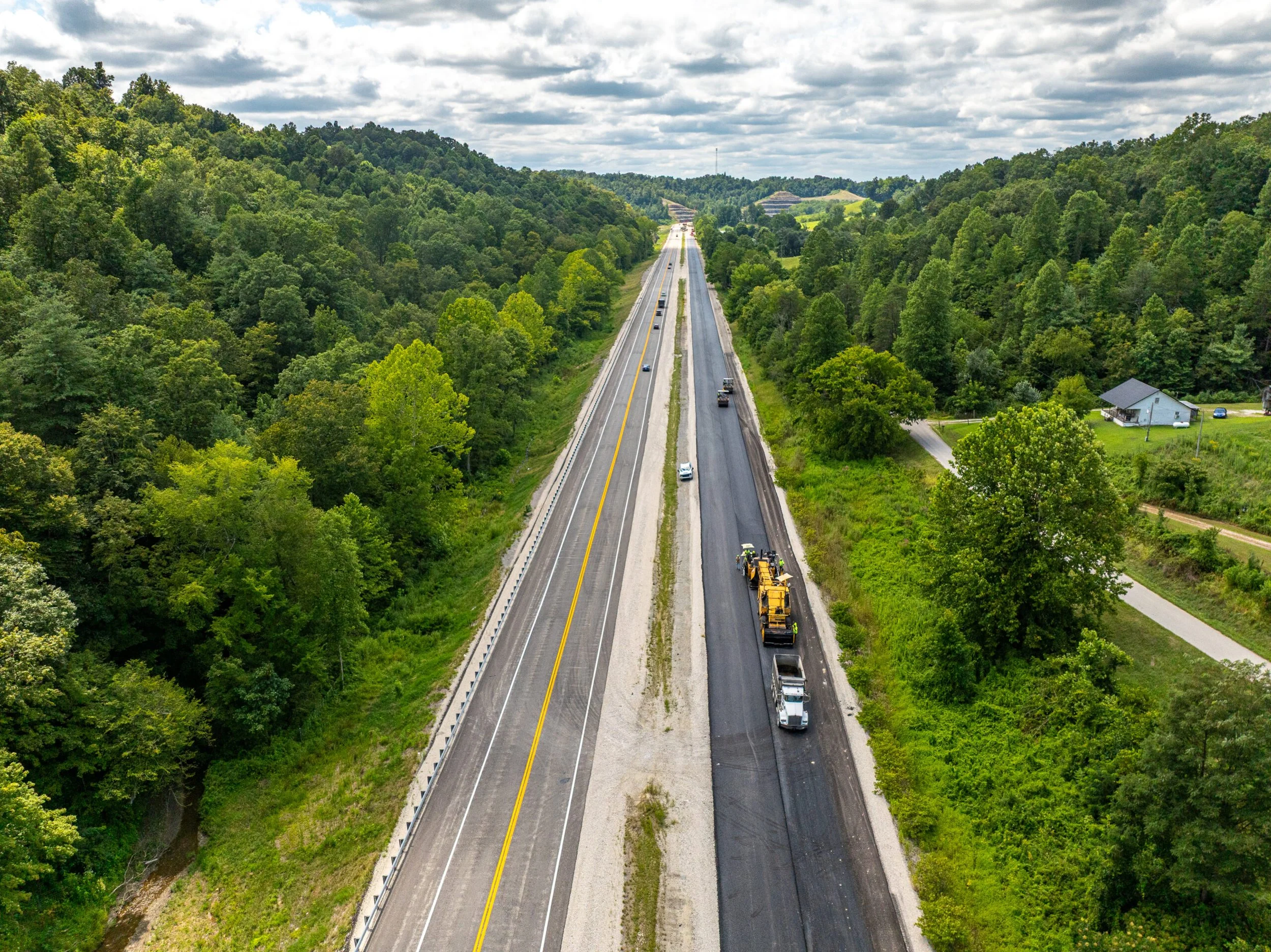 Tree lined mountains split by the four-lane highway. Construction works can be seen repaving one half of the highway