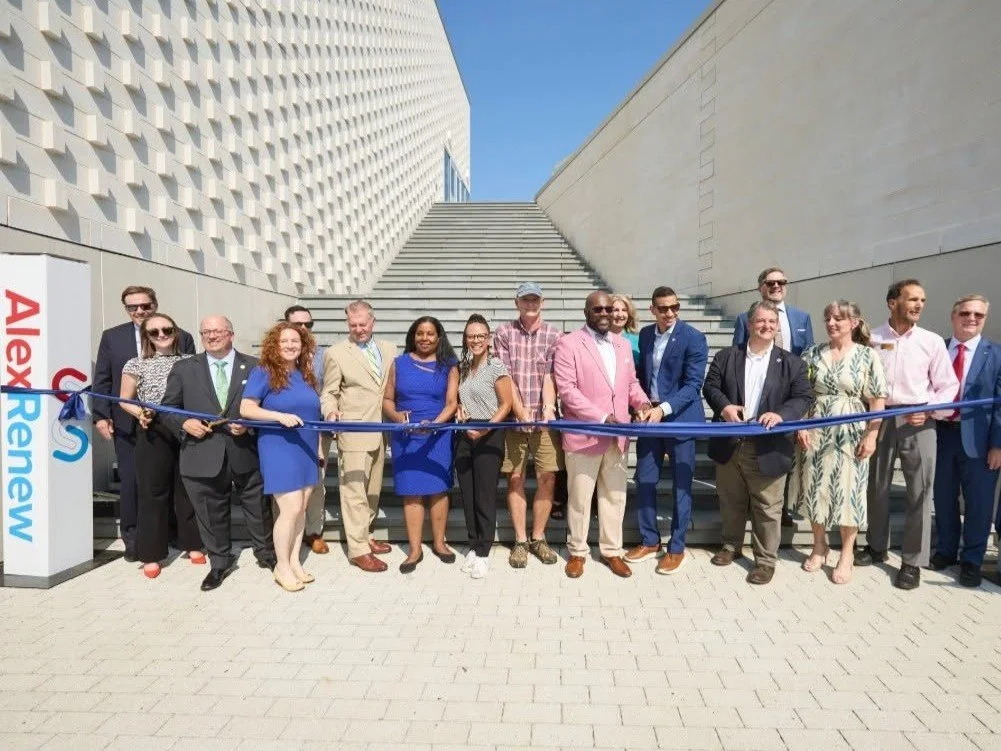 Alexandria, VA Mayor Alyia Gaskins and others stand at the bottom of some stair outside of the AlexRenew building, preparing to cut a ribbon.