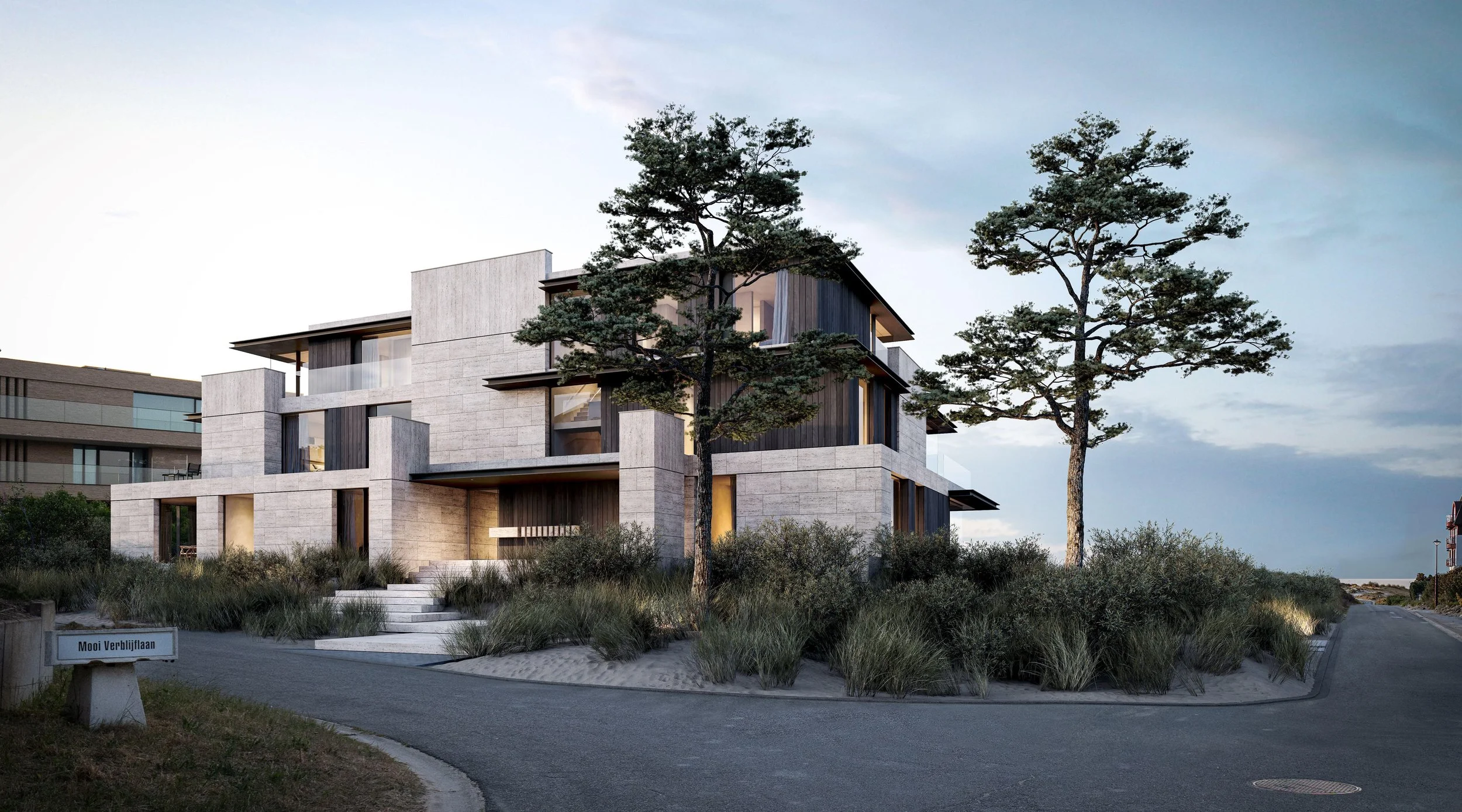 Modern multi-story house with large windows and a combination of light and dark exterior materials, surrounded by trees and shrubs, under a partly cloudy sky.