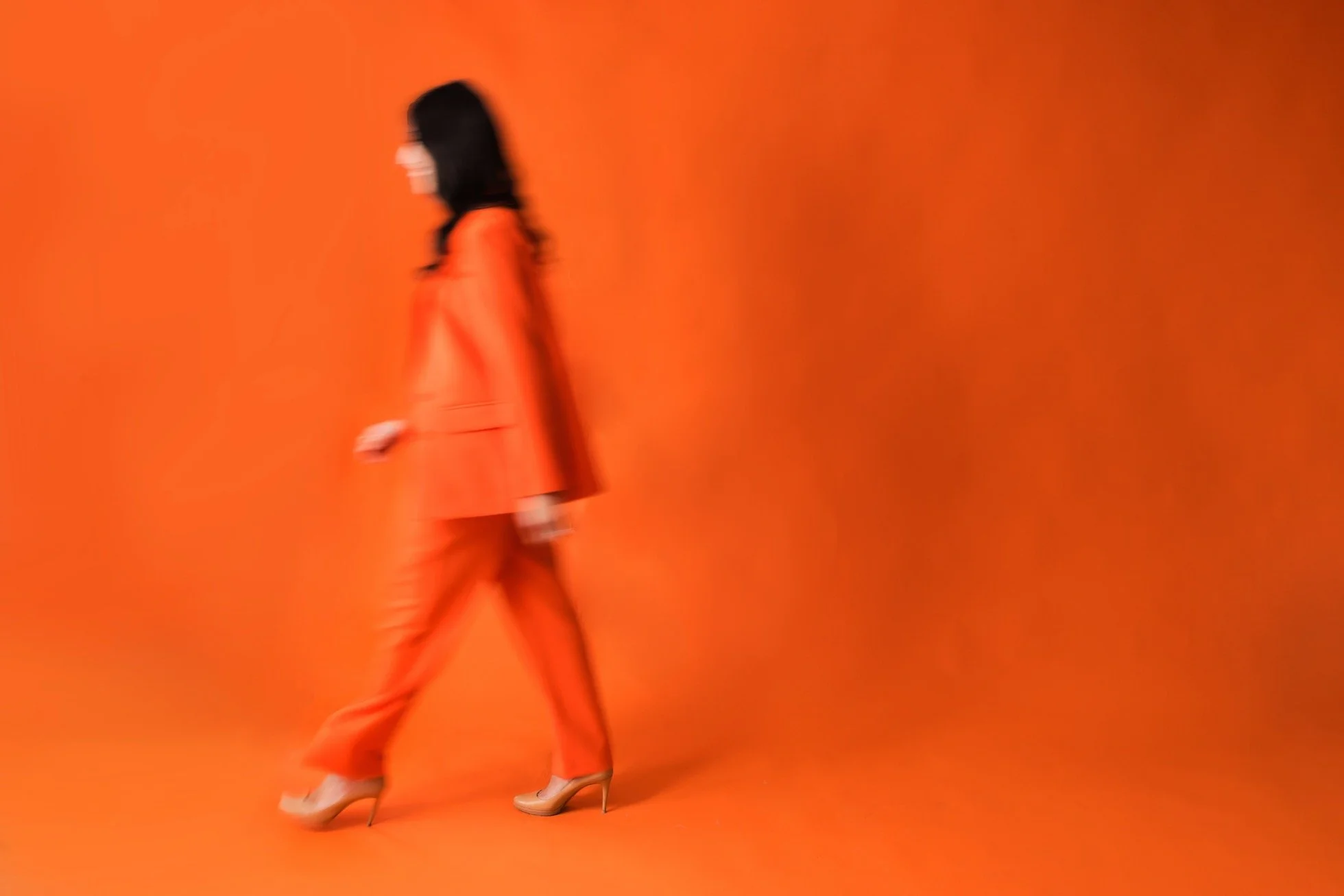 Erica Orange walking in an orange suit against an orange backdrop