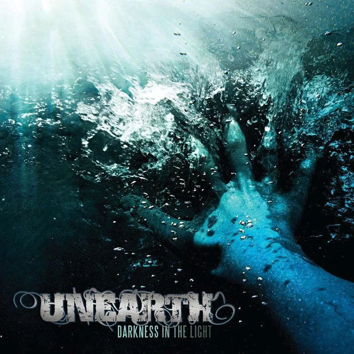 A hand reaching into dark water with bubbles and light shining from above, with the text 'Unearth Darkness in the Light' at the bottom. Album artwork.