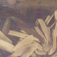 A collection of unfinished wooden furniture parts and boards in a workshop or storage area. Album art.