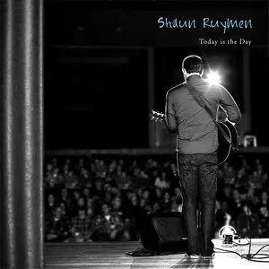 A man playing a guitar on stage during a performance, with a crowd in the background, in black and white. Album art for "Today is the Day" by Shaun Ruymen.