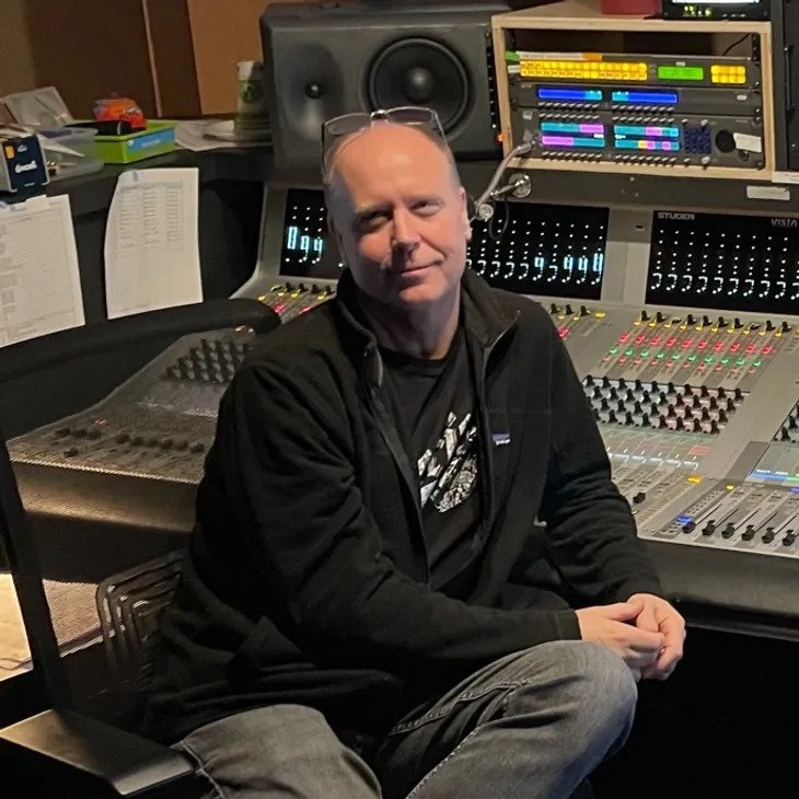 Man sitting in a recording studio with audio mixing equipment and speakers.