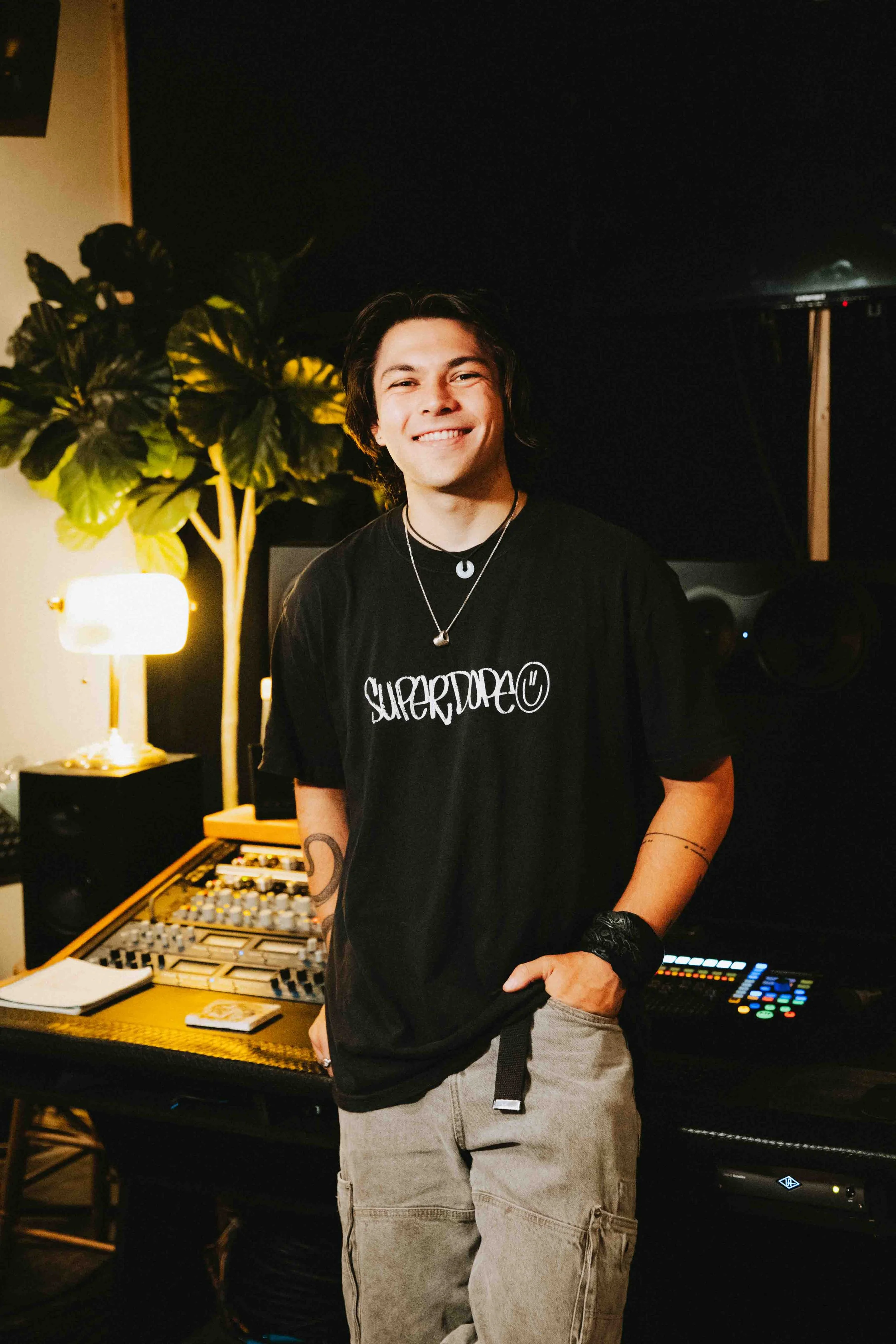 David Stingle sitting in a recording studio surrounded by sound equipment, mixing console, large speakers, and music production software on screens.