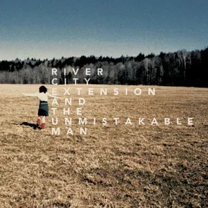 A person standing on a grassy field near a river with trees in the background, with text overlaid that says 'River City Extension and the Unmistakable Man'. Album art.