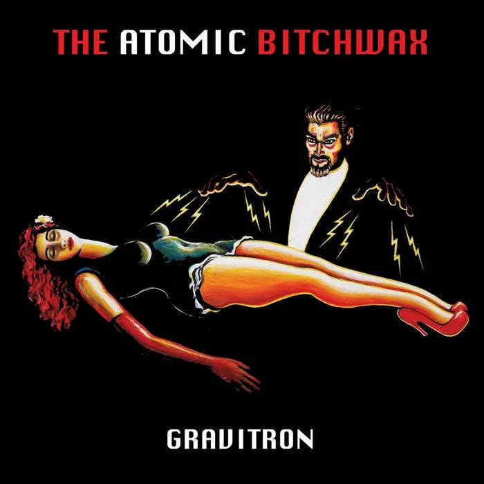 Illustration of a man with lightning around his hands holding a woman lying down with red hair, a black dress, and red boots. The text reads 'THE ATOMIC BITCHWAX' at the top and 'GRAVITRON' at the bottom. Album artwork.