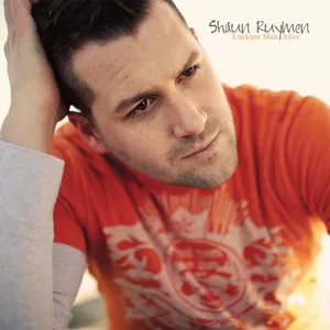 Portrait of a man with dark hair, wearing an orange T-shirt with a graphic design, looking thoughtful with his hand resting on the back of his head. Shaun Ruymen ALbum art.