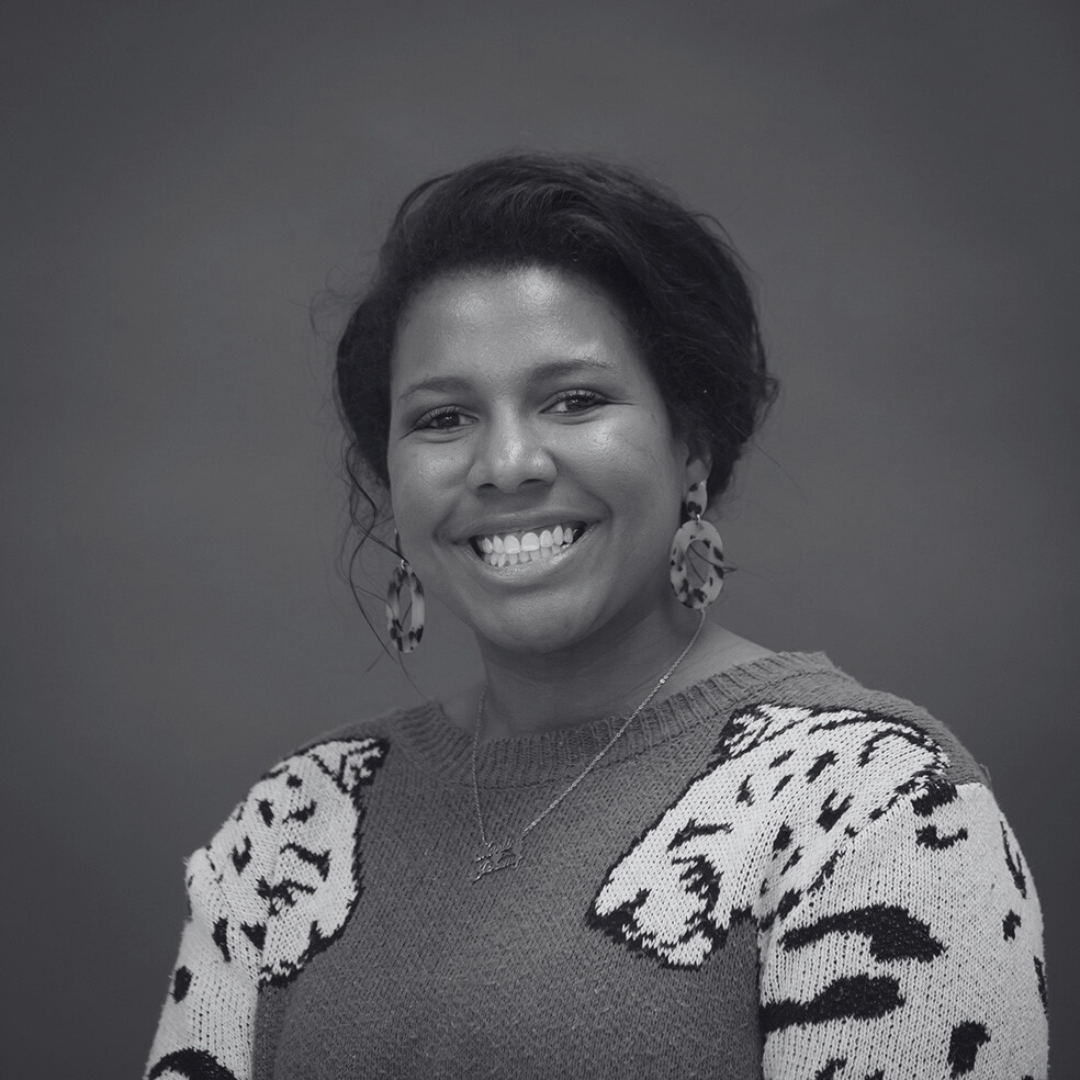 A smiling person wearing a sweater with animal patterns and large hoop earrings in a grayscale portrait.