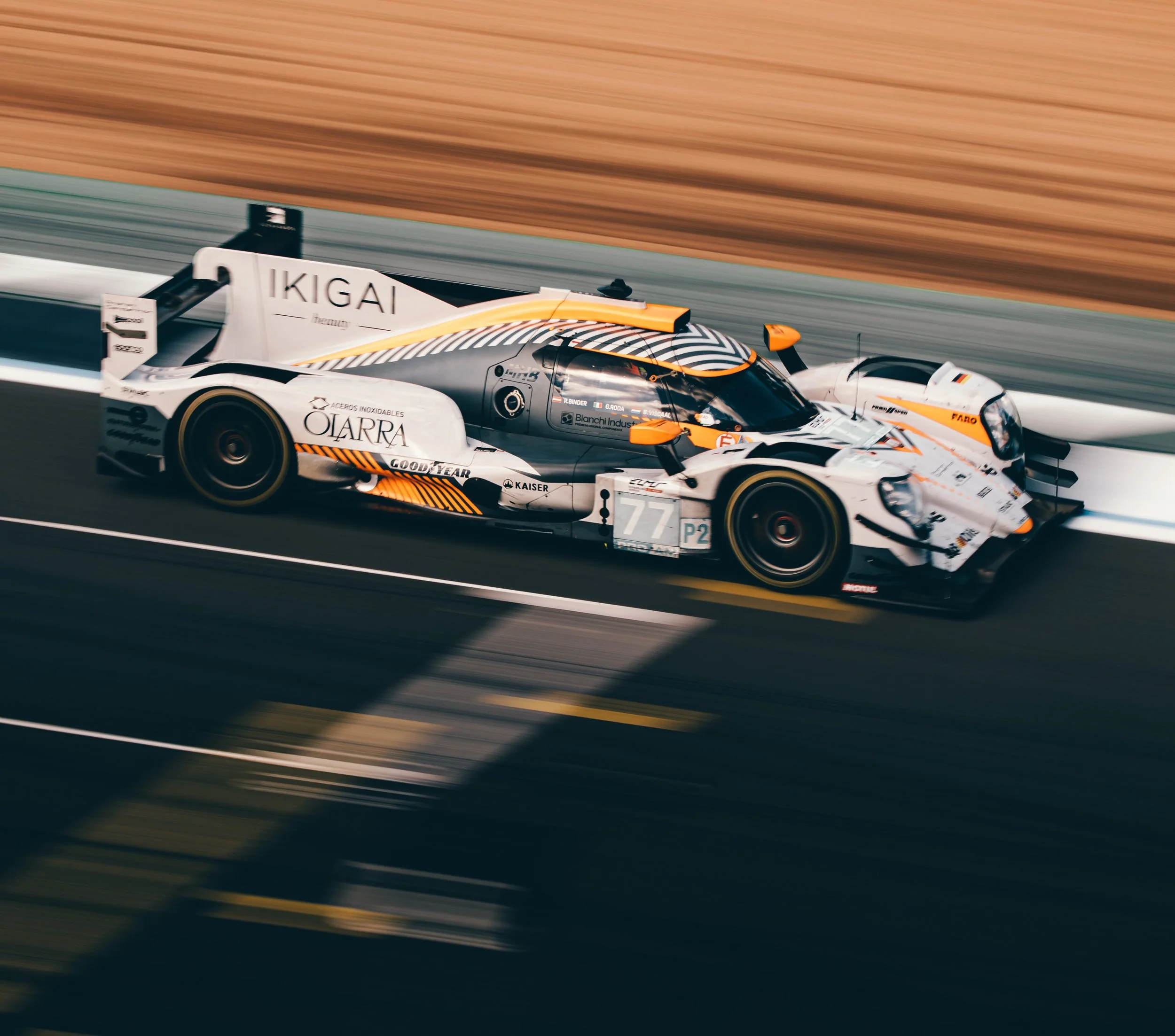 Race car on a racetrack, white with black and orange accents, moving fast with motion blur.