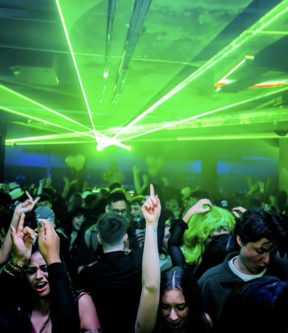 Crowd of people dancing and enjoying themselves at a nightclub with green laser lights overhead.