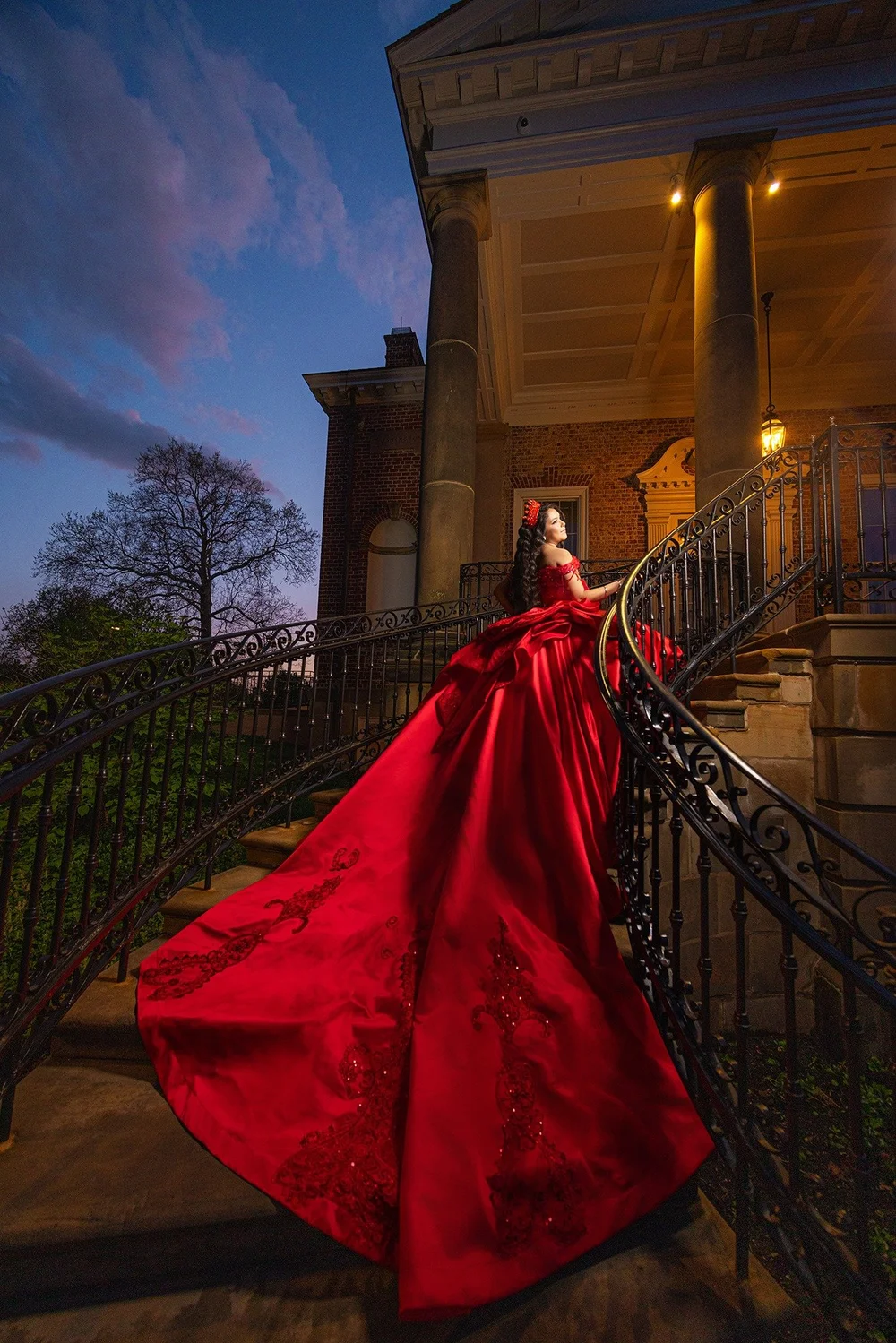 Quinceañera wearing a red gown on a historic staircase at dusk