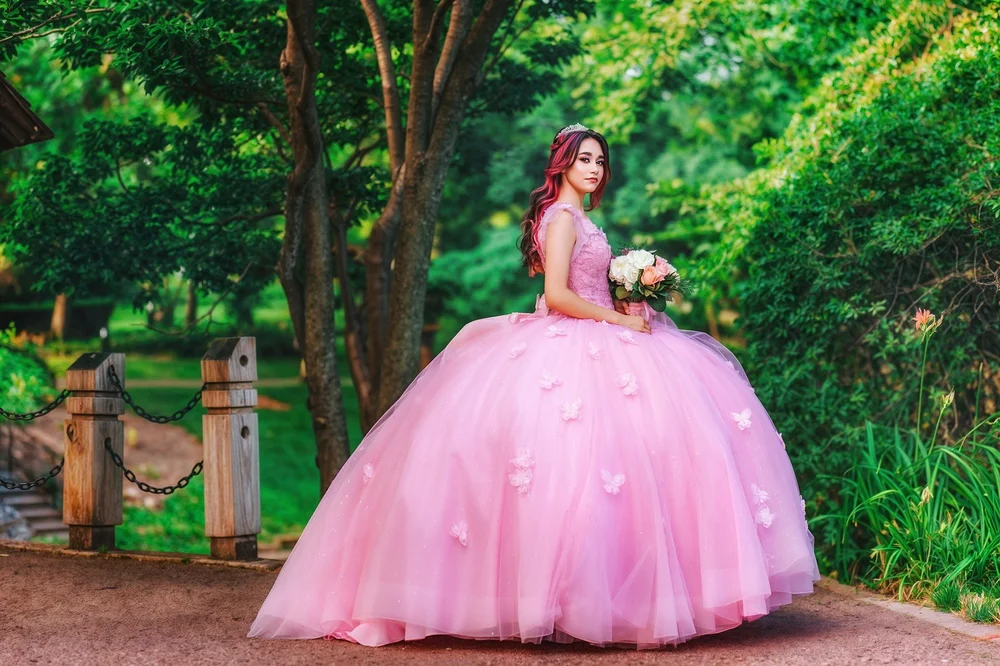 Abby in a pink quinceañera gown holding a bouquet in a green outdoor setting