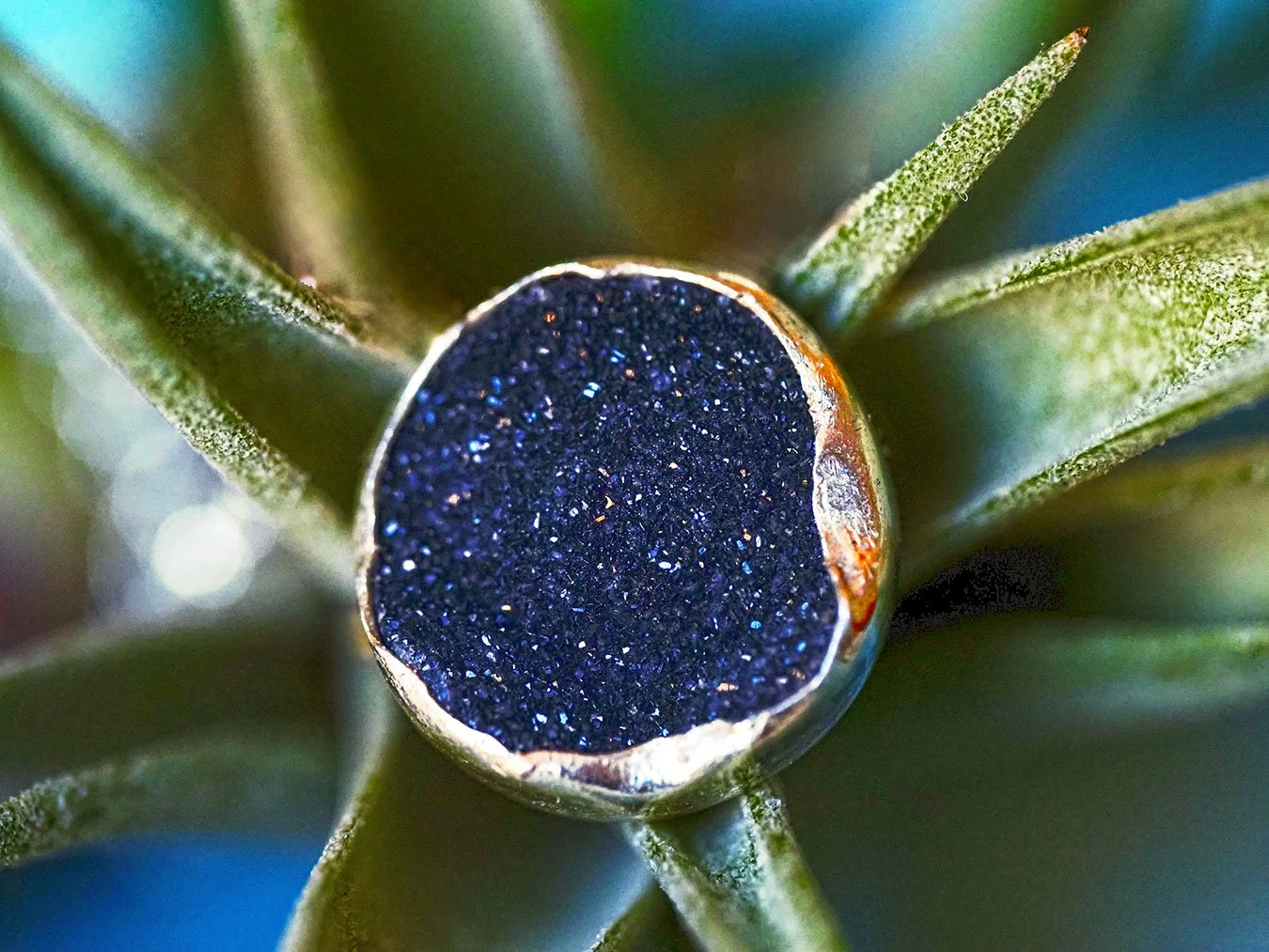 Fine art product photograph of a silver black druzy stone, captured in close detail to emphasize its natural crystalline structure and subtle sparkle. The image highlights deep charcoal tones, metallic edges, and texture, presented against a softly b