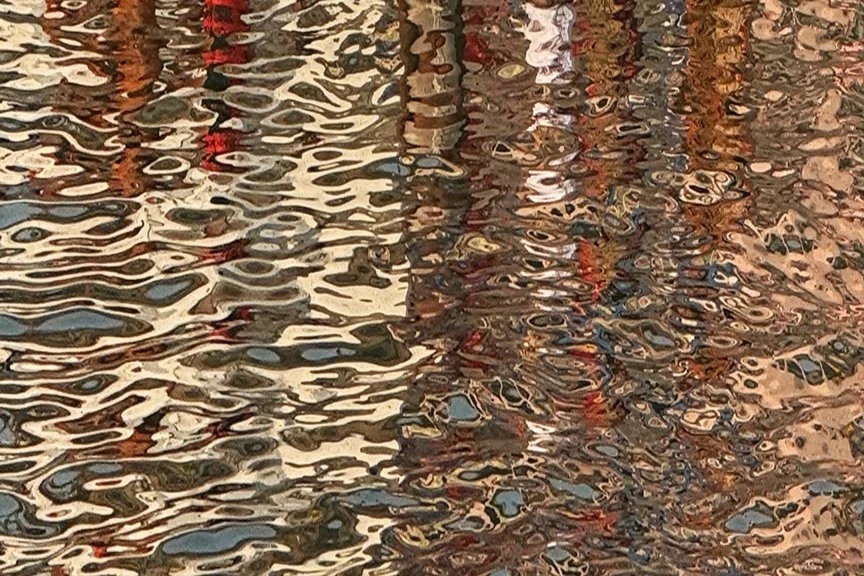 Reflections of boats and structures on water with ripples and distorted reflections.