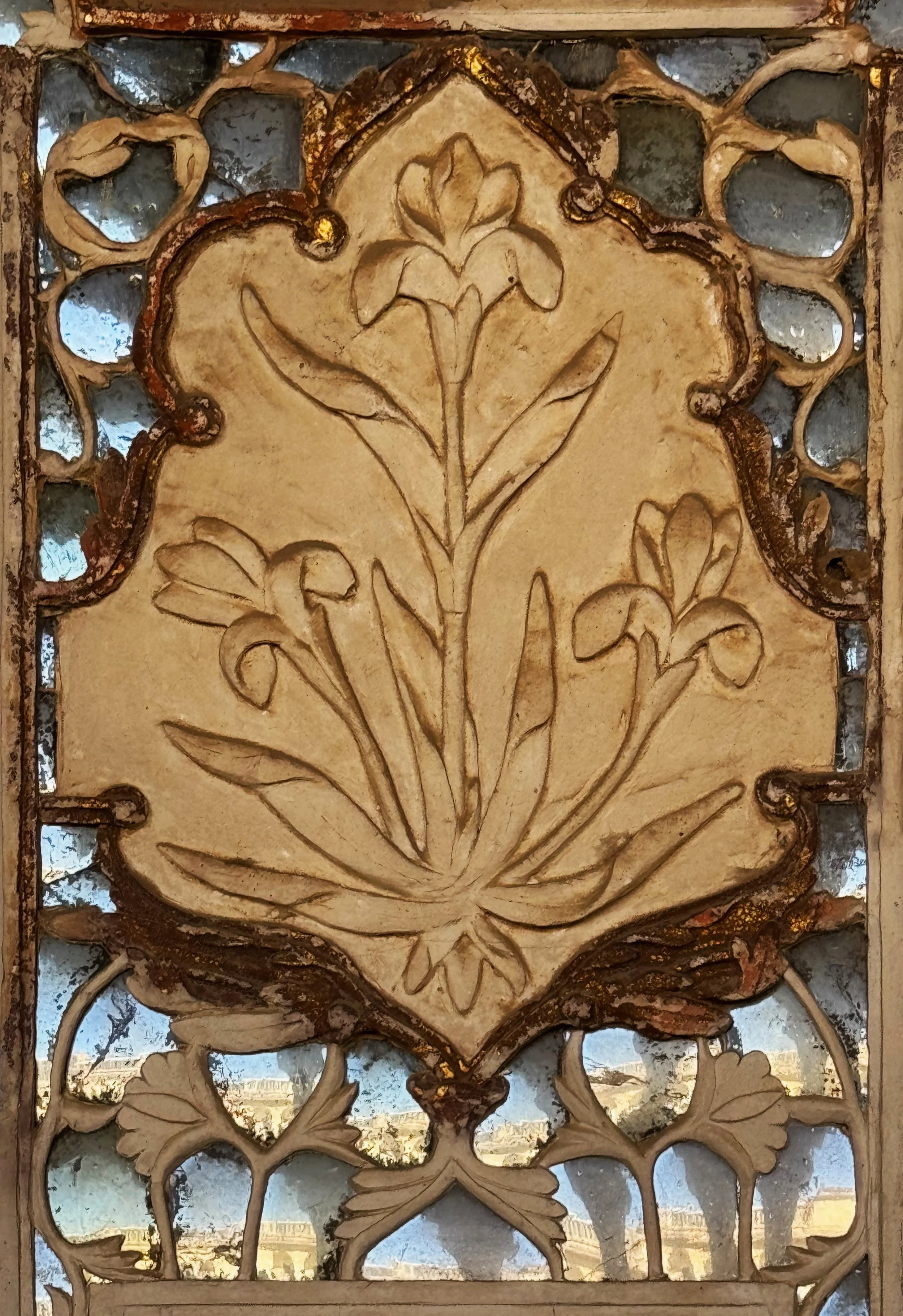 Intricate carved wooden panel with floral and decorative patterns, with a scenic view of a cityscape and river through the openings.