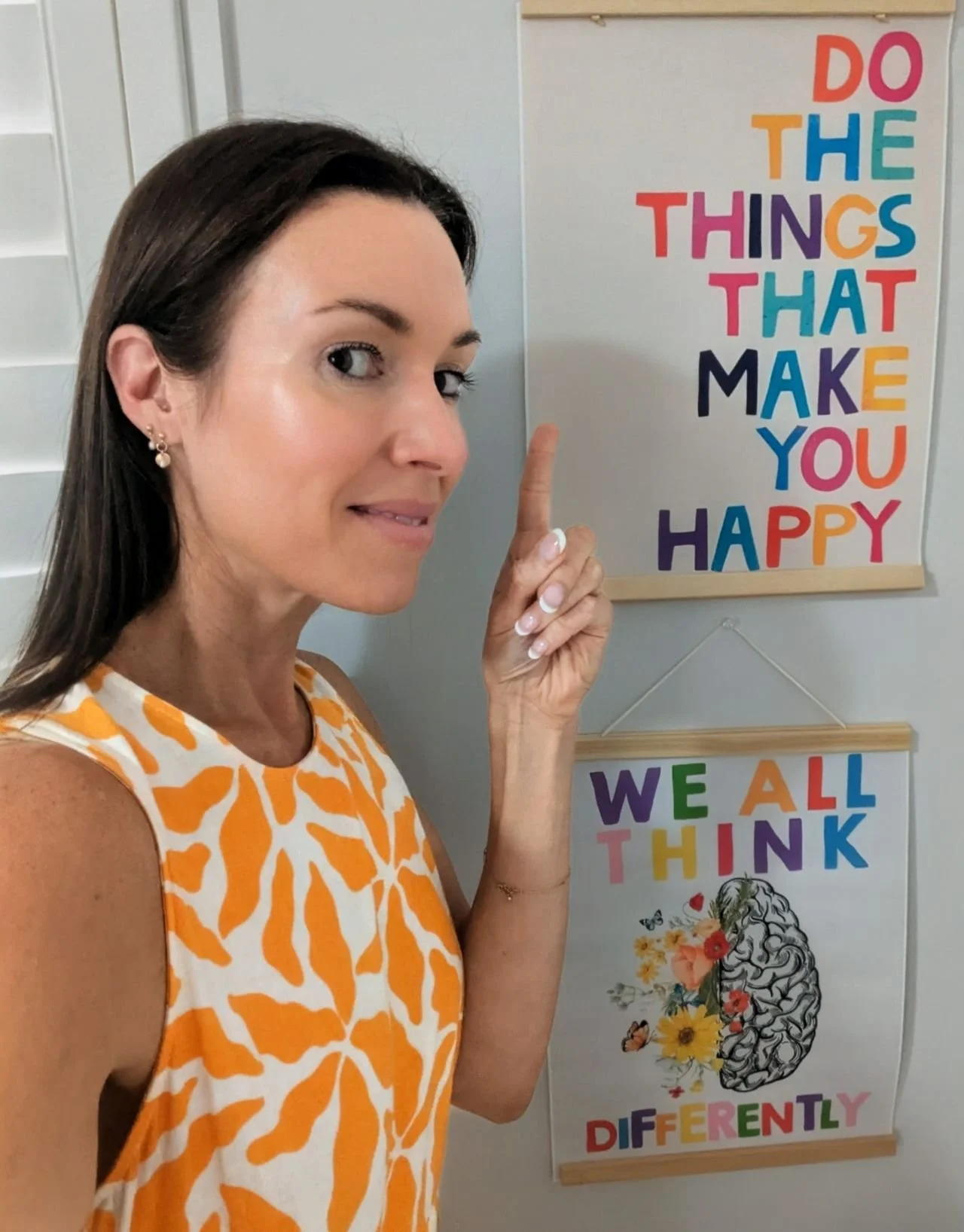 Women with shoulder length brown hair wearing a yellow dress is pointing to a sign which reads "DO THE THINGS THAT MAKE YOU HAPPY" AND "WE ALL THINK DIFFERENTLY"