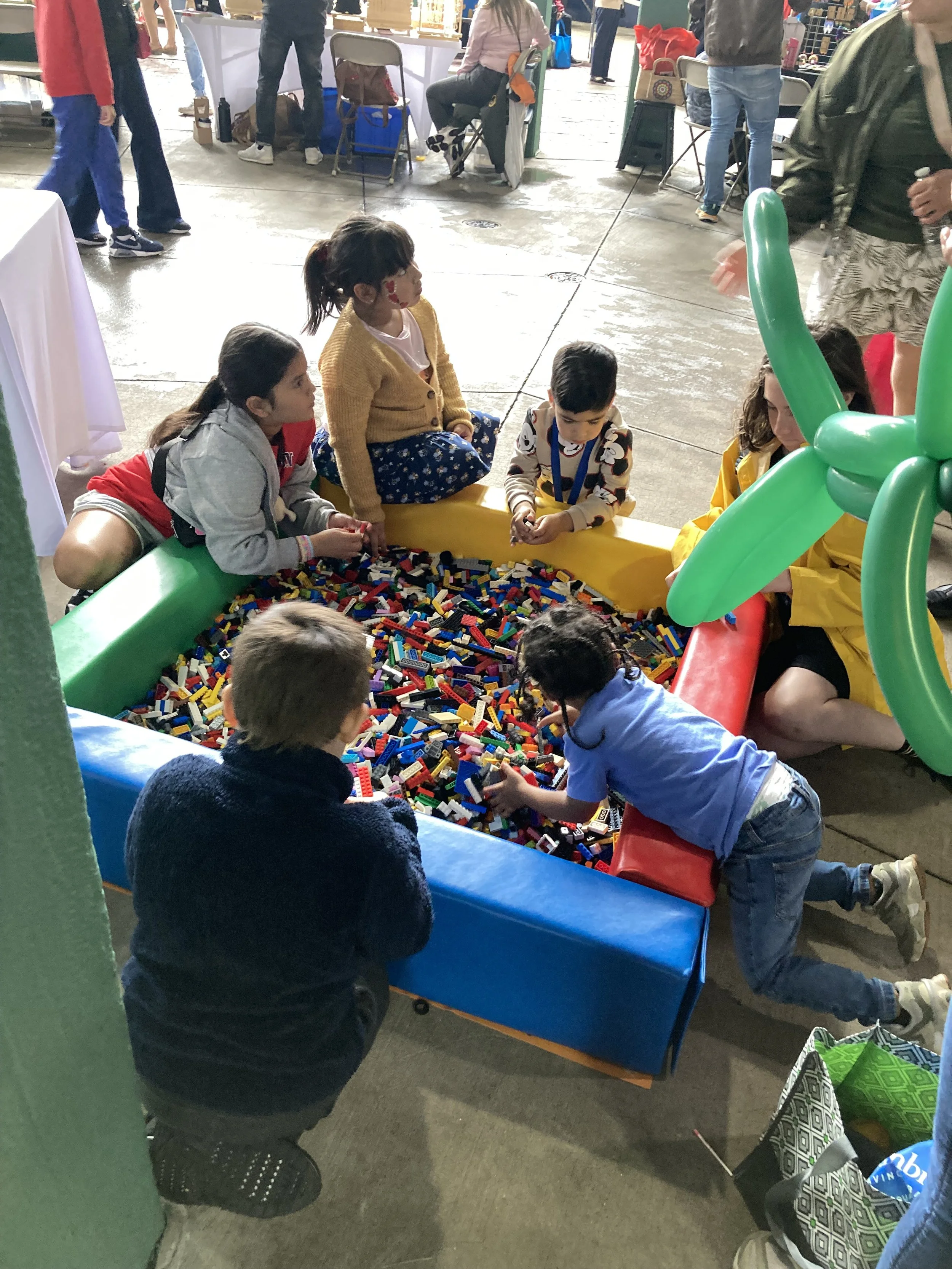 Children playing with LEGO bricks in a small play area at a public event.