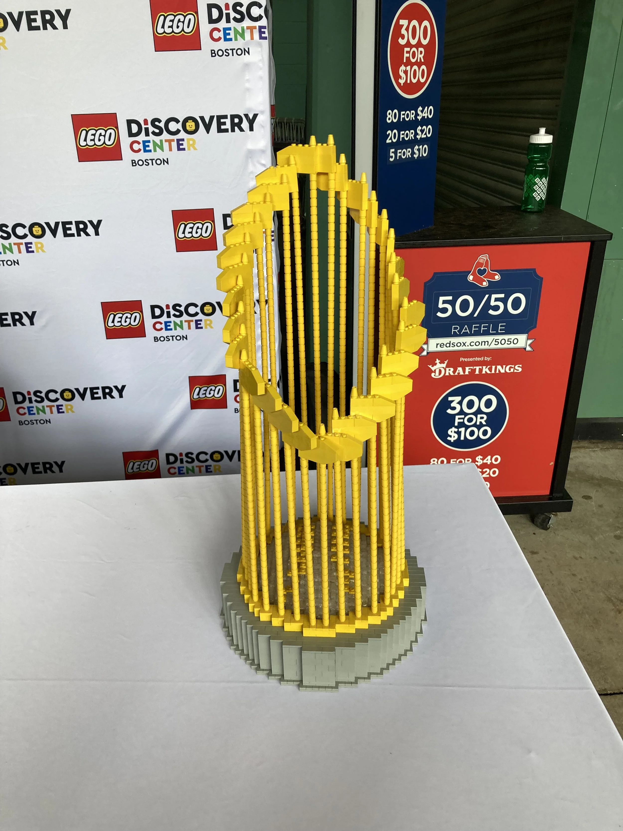 Lego model resembling a championship trophy displayed on a table at a Lego Discovery Center event, with raffle information visible in the background.