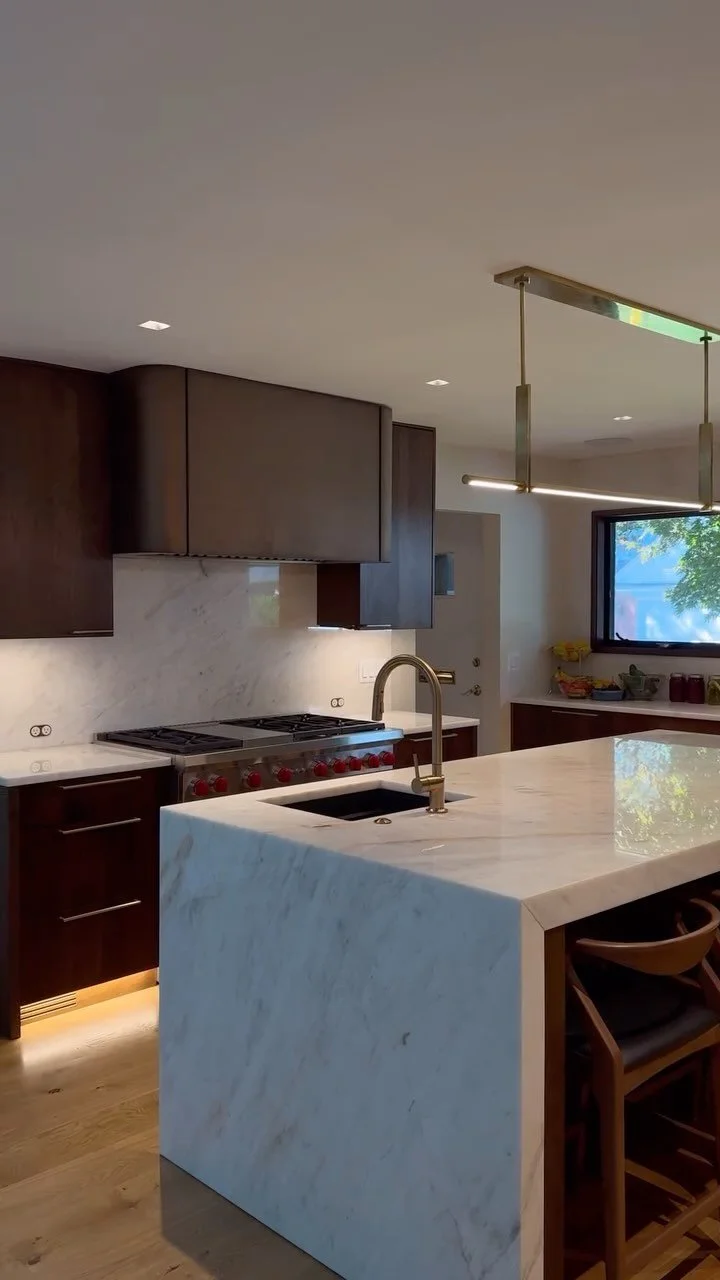 With moody, contemporary influence this rich walnut kitchen comes to life with layers of soft lighting and carefully designed detail. Adding depth, the cristallo countertop veining accents the deep brown cabinetry finished with a custom faux metal ho