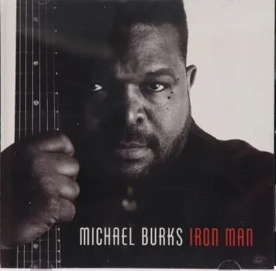 Close-up of Michael Burks holding an electric guitar next to his face, with album title 'Iron Man' displayed.