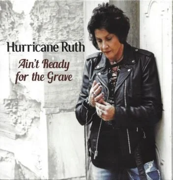 Album cover for Hurricane Ruth's "Ain't Ready for the Grave" featuring a woman with dark hair wearing a black leather jacket, standing against a weathered wall.