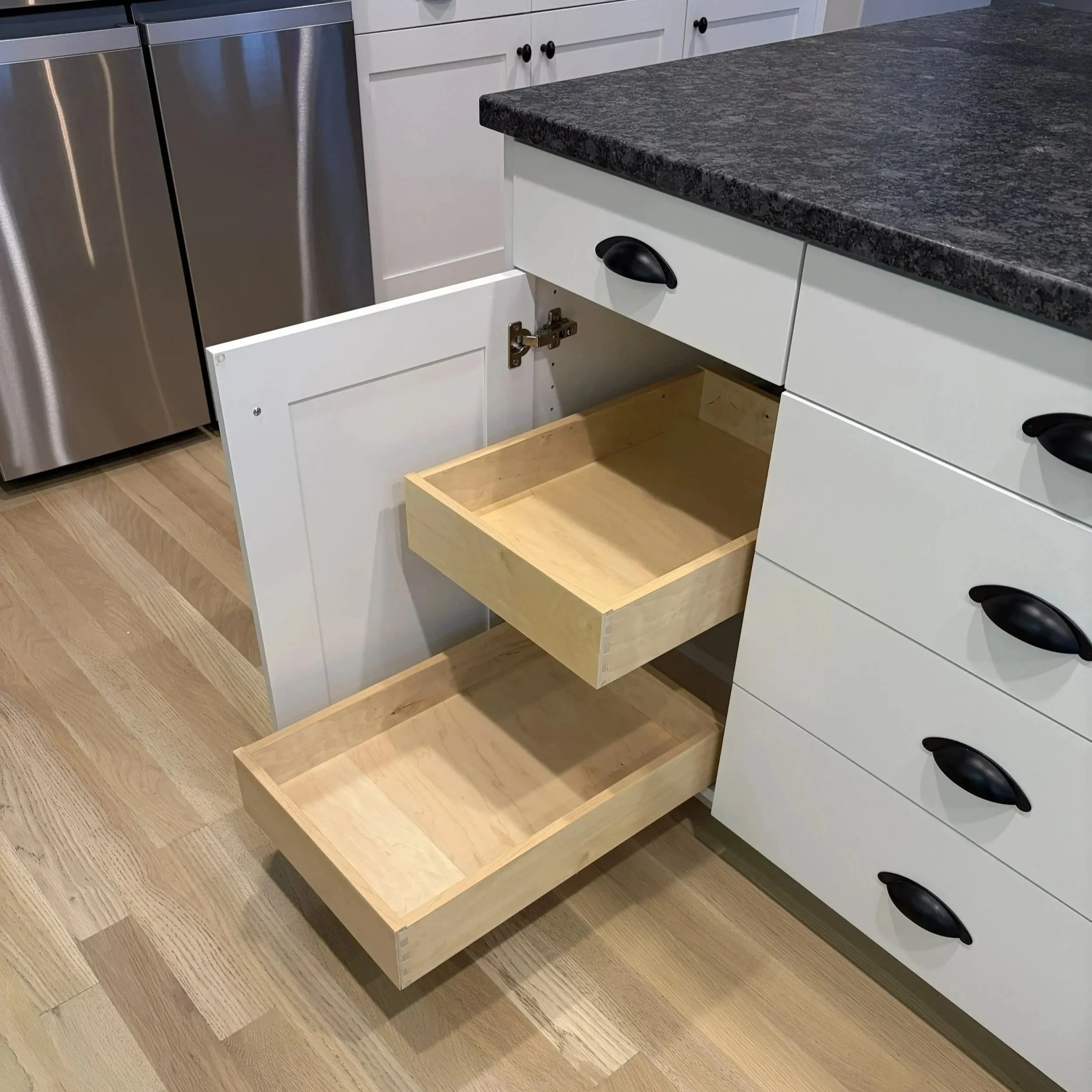 two wood pullout drawers half open extending from a white kitchen cabinet