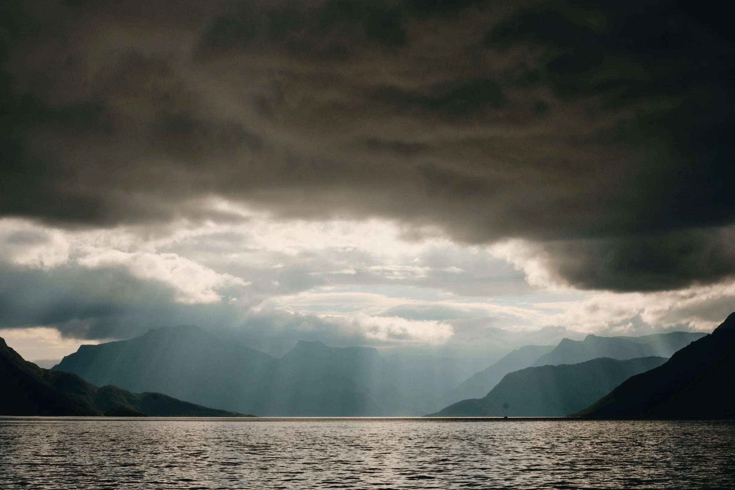 A dark, cloudy sky over a mountain landscape with a large body of water in the foreground.