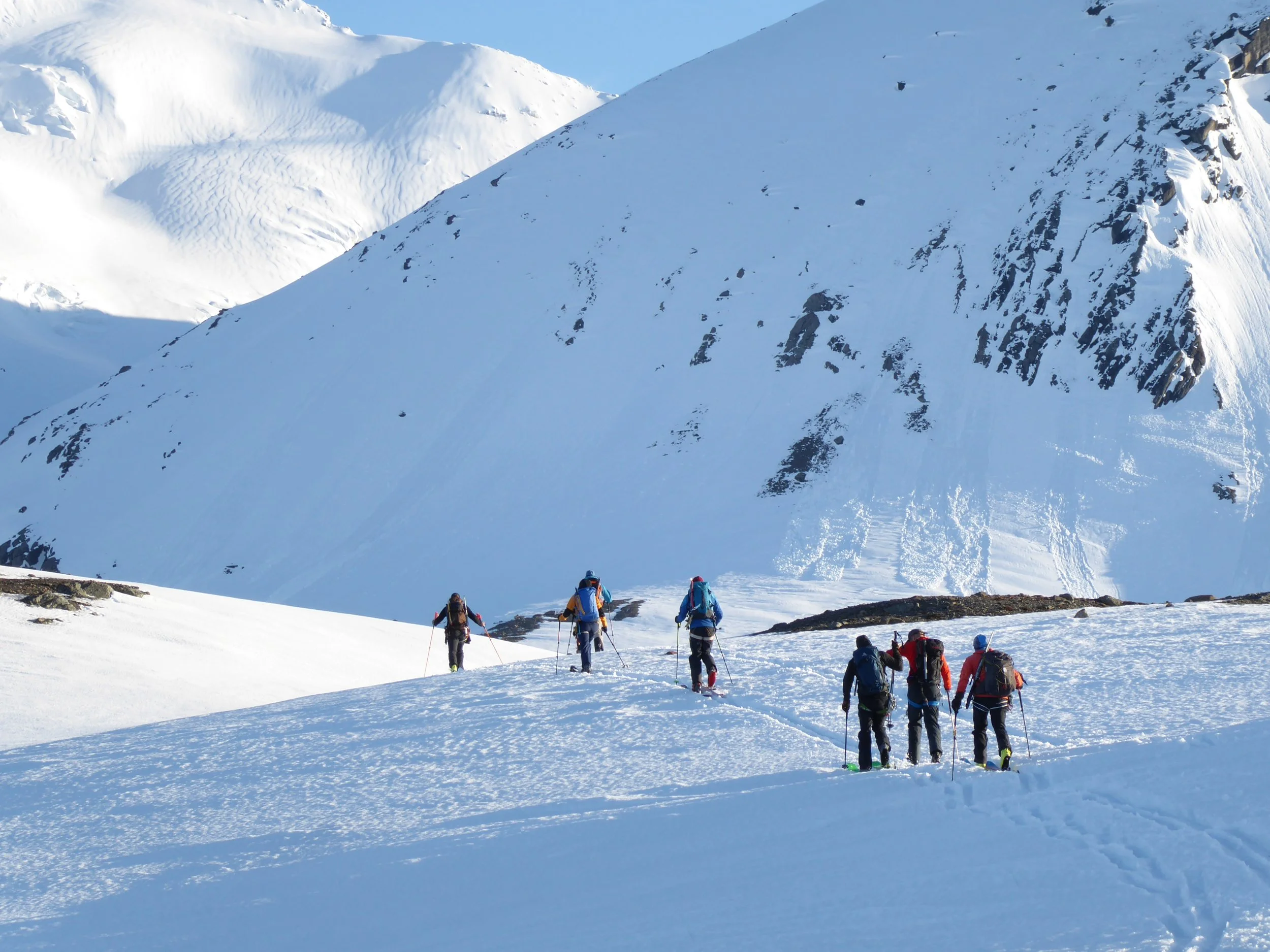 An expedition group walking in snow covered mountains in Svalbard on a sunny day.