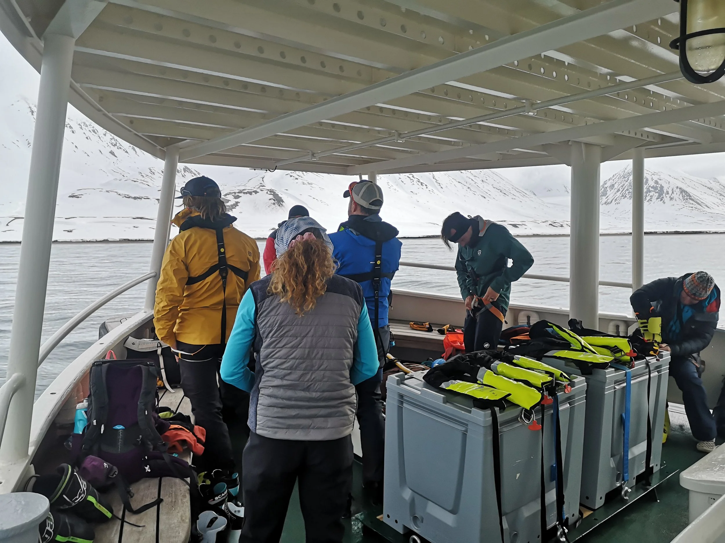 People on a boat preparing gear with snowy mountains in the background.