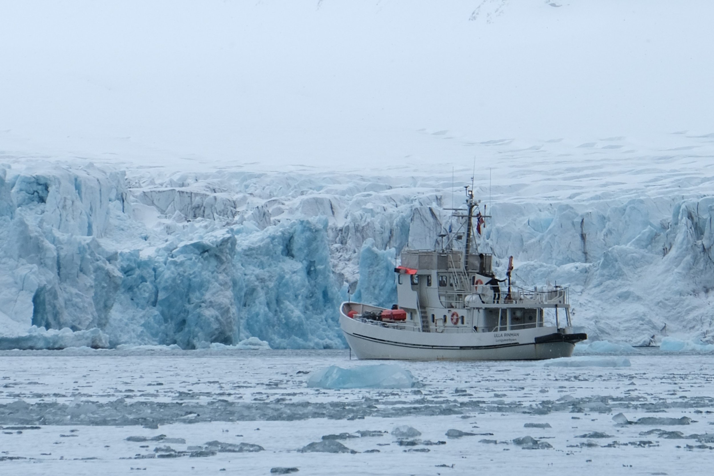 A boat sailing in icy waters near a glacier with icebergs and ice floes
