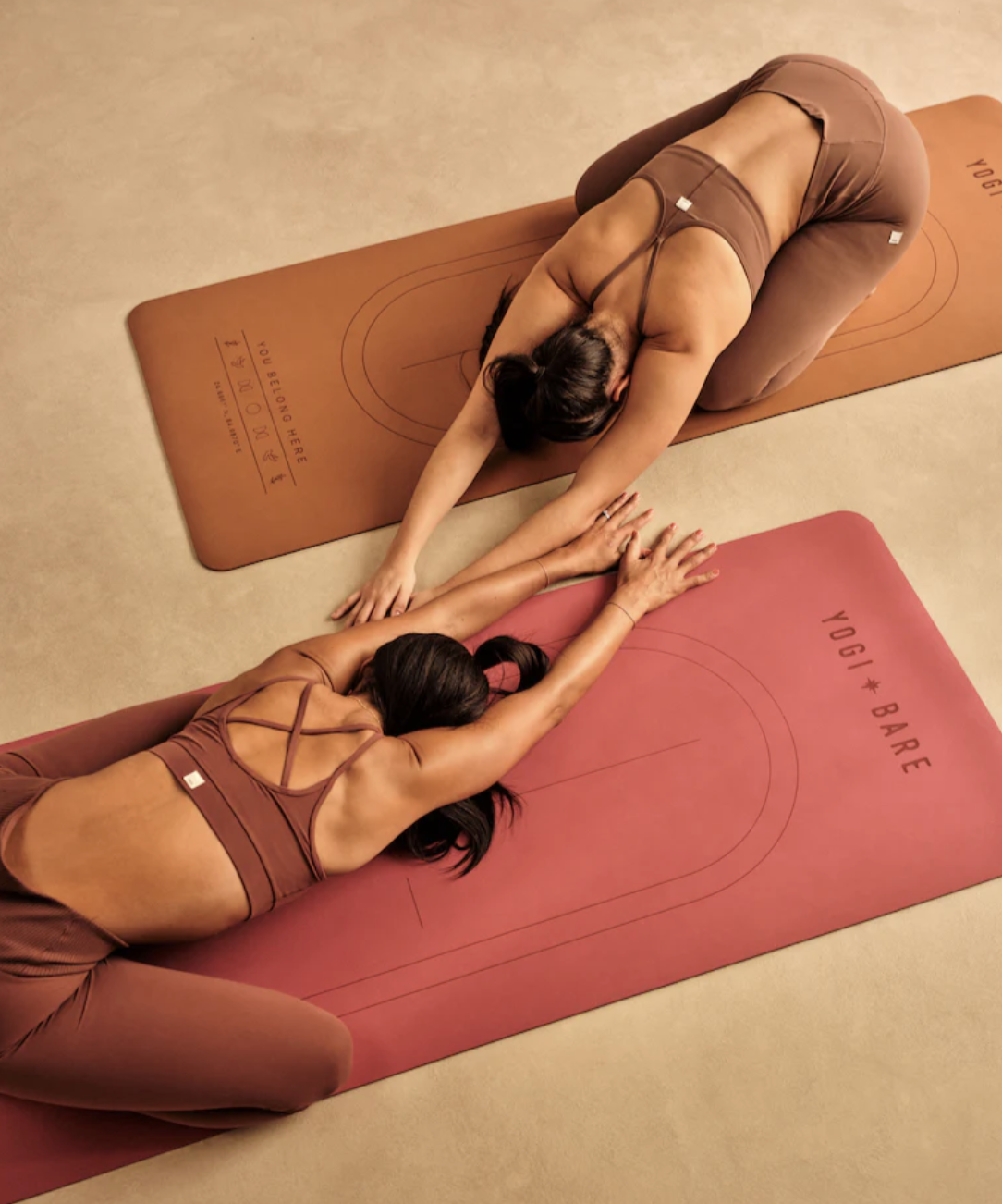 Two people practicing yoga on mats, positioned in child's pose, wearing matching workout outfits.
