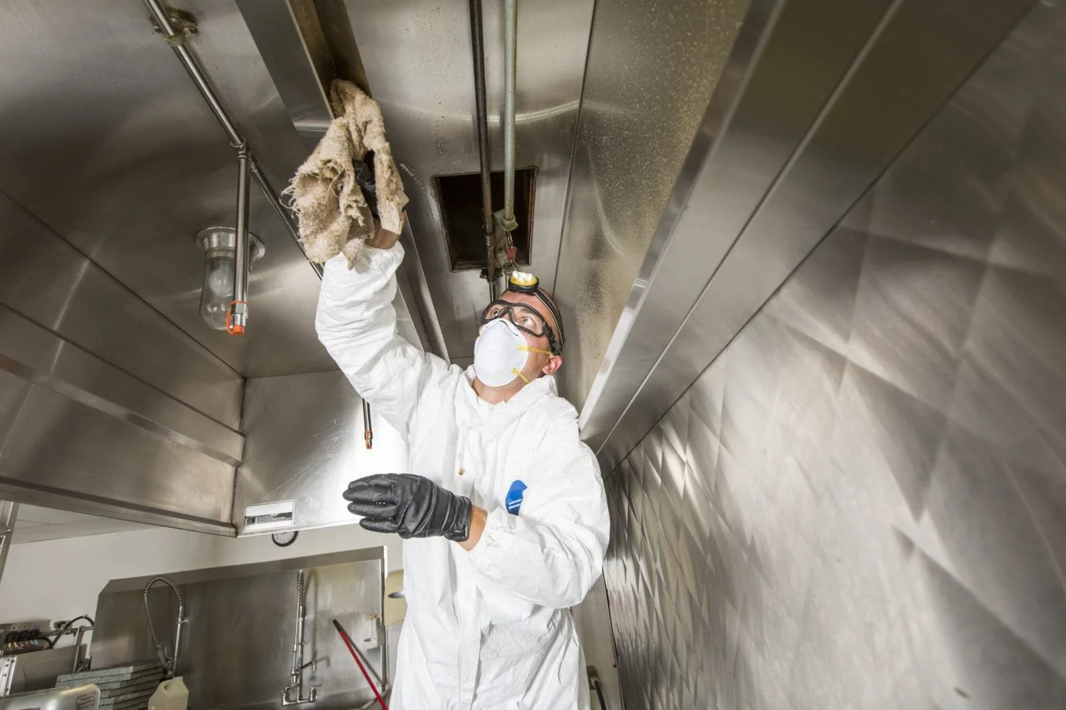 Worker in protective gear cleaning commercial kitchen exhaust