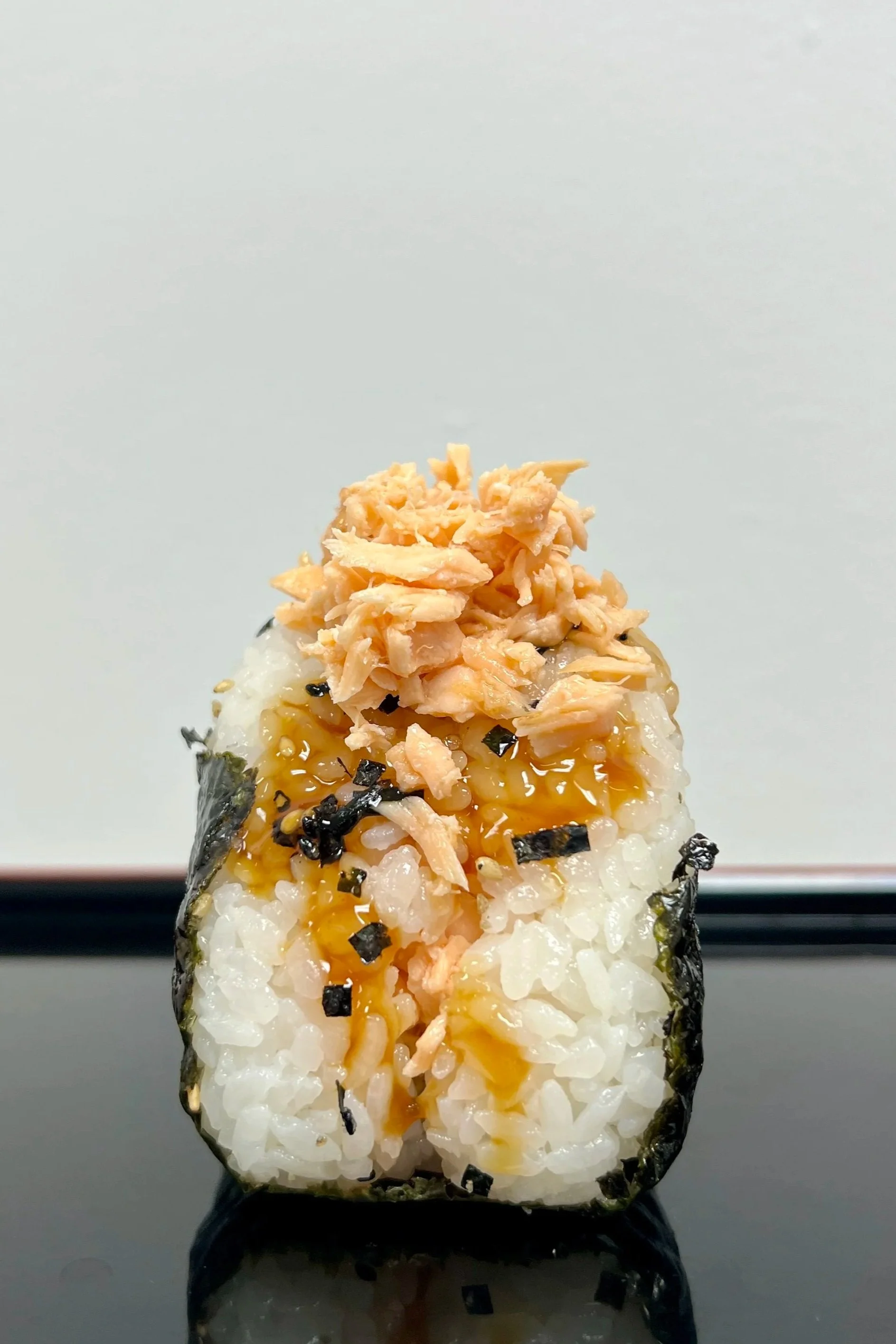 Close-up of a salmon teriyaki onigiri rice ball with shredded salmon on top, drizzled with  teriyaki sauce, best seller! 