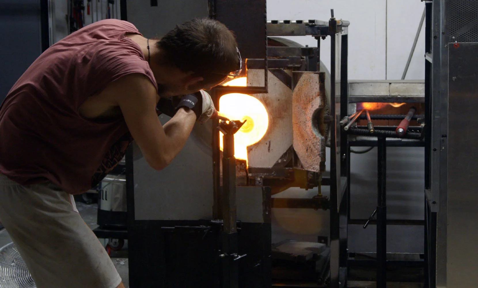 A glassblower working with molten glass in a furnace.
