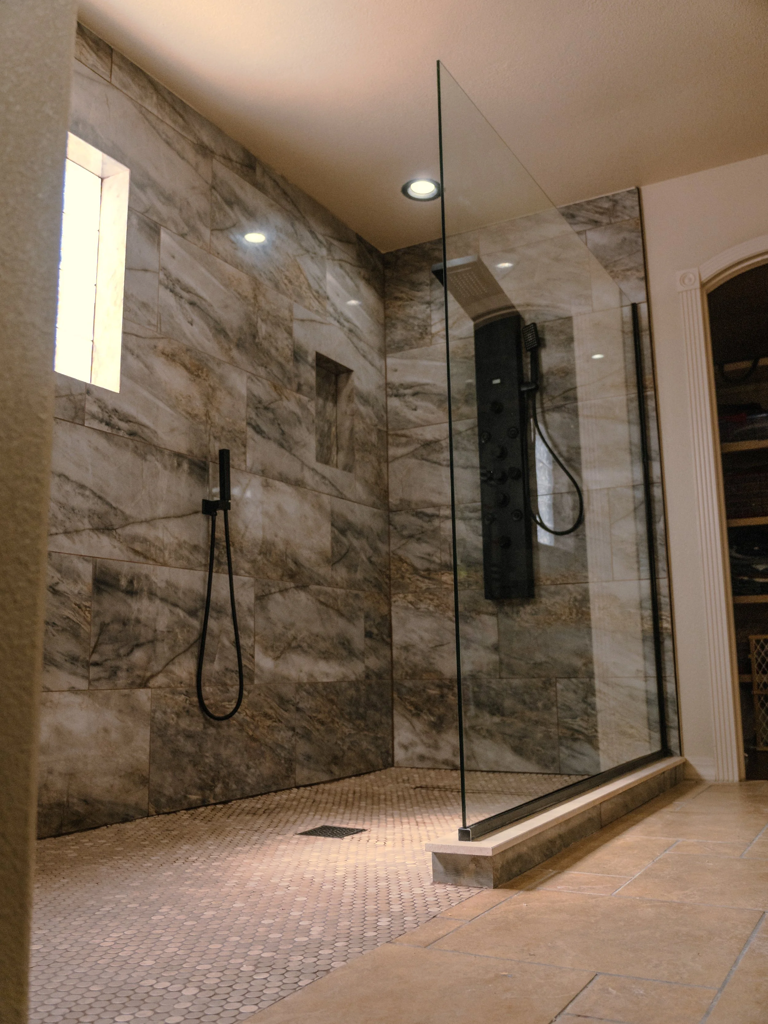 Small bathroom with marble tile walls, a mirror, a small window, and a vanity light fixture.