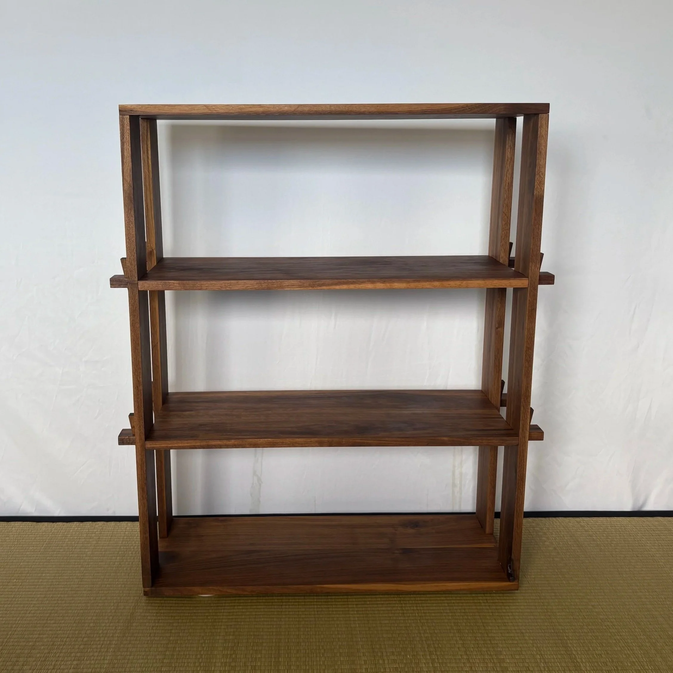 Empty wooden bookshelf against a plain wall with a brown carpeted floor.