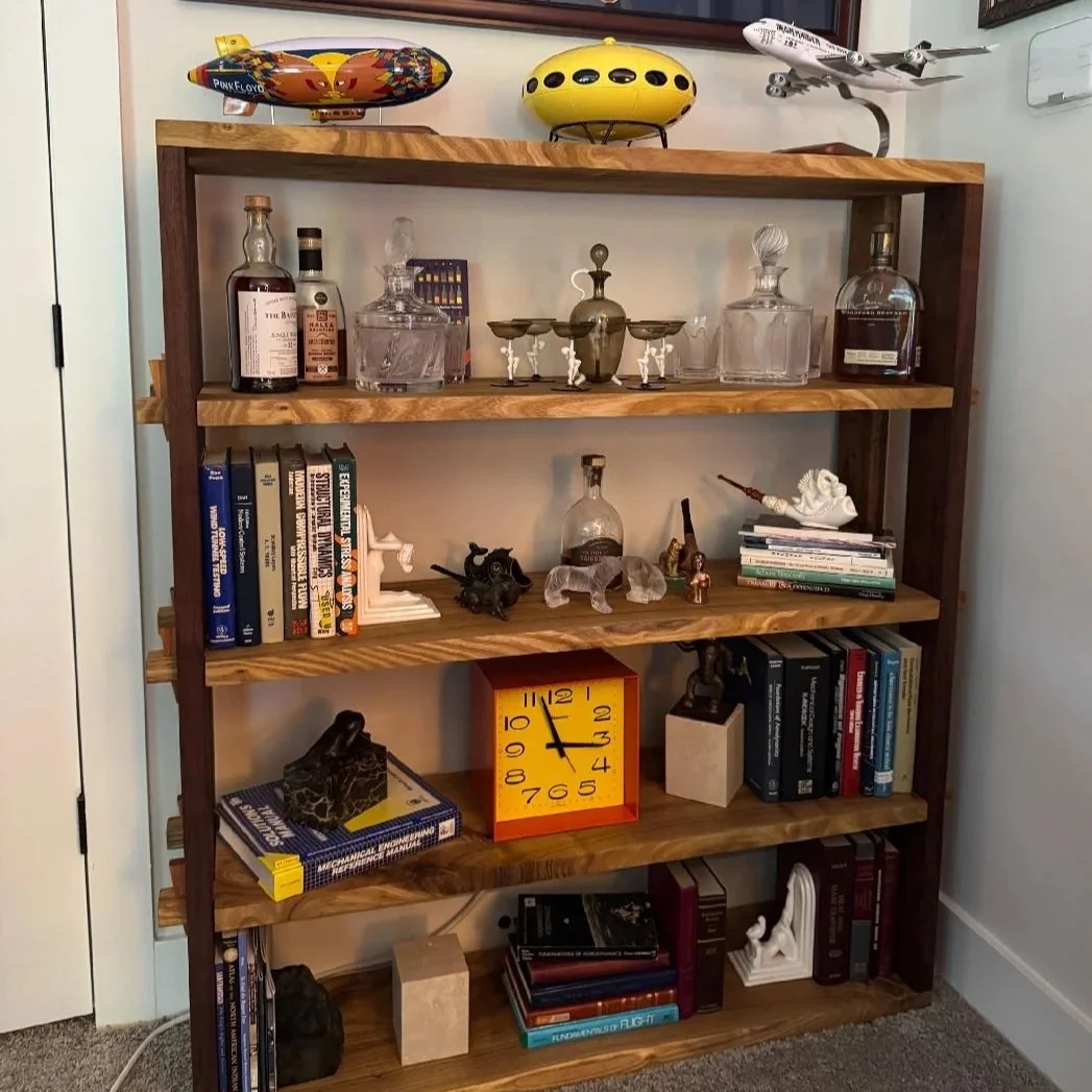 A wooden bookshelf filled with books, decorative items, and small models, with model airplanes on top.