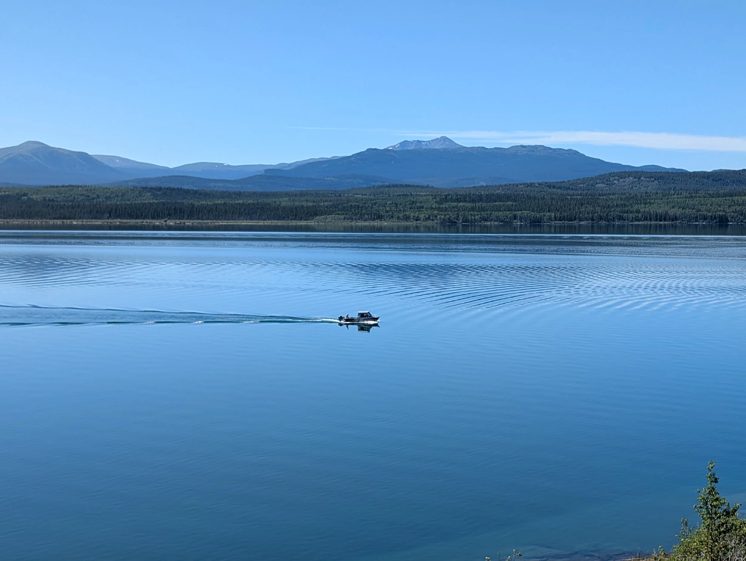 Boat crossing calm lake, deep blue water forested mountains background. 
