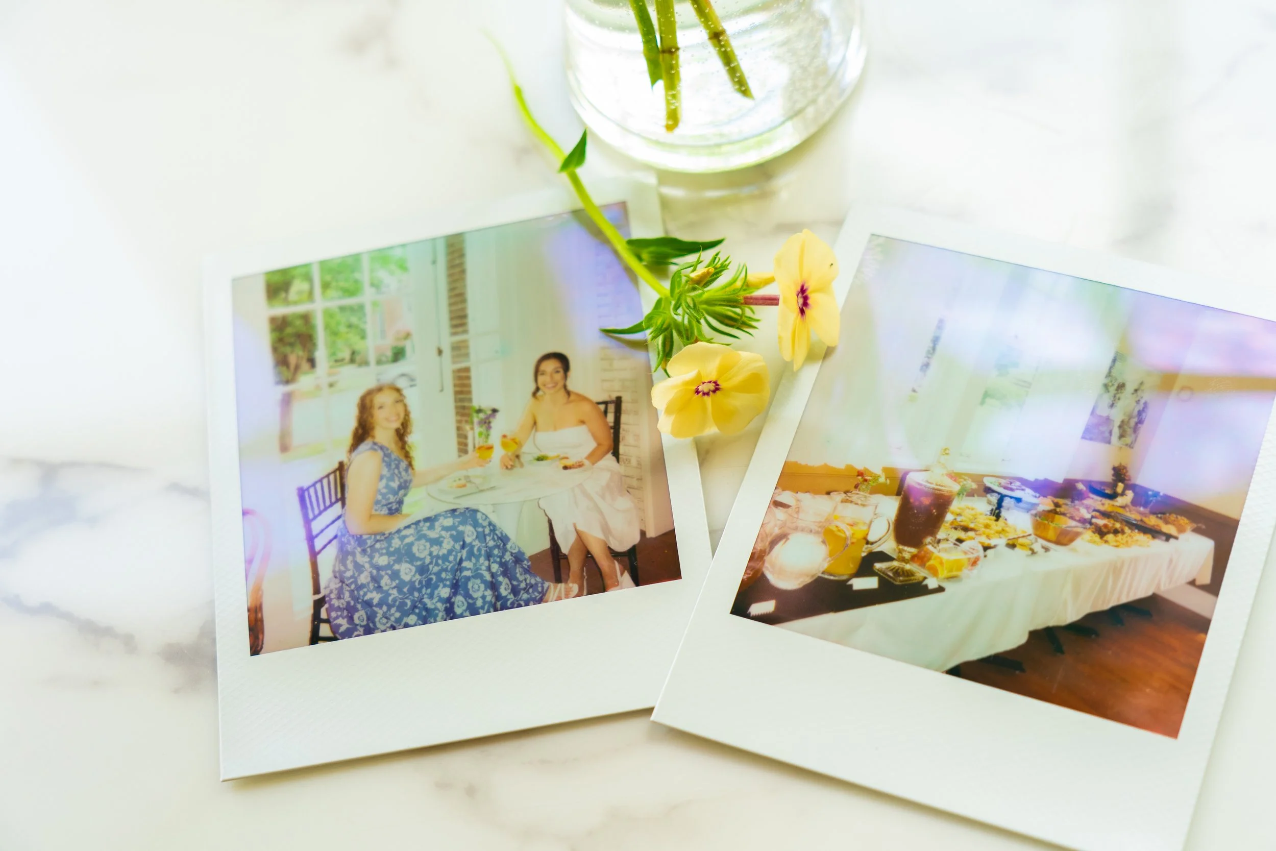 Polaroid photos of a brunch gathering on a white surface with a small yellow flower and a glass vase with water and green stems.
