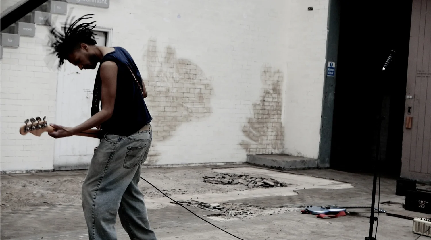 A guitarist playing against an exposed brick wall at The Generator