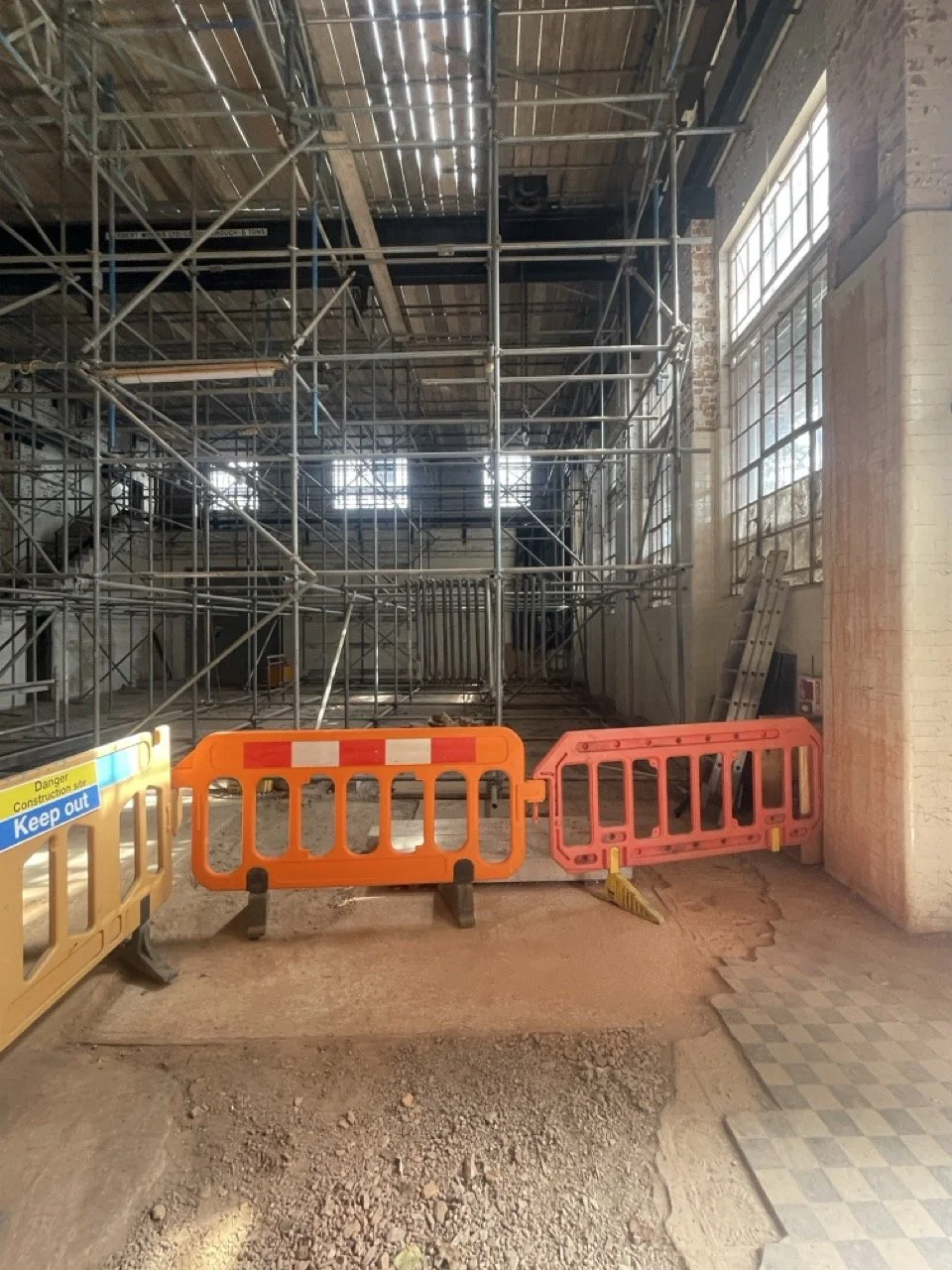 Indoor construction site with scaffolding, orange and yellow safety barriers, and a sign that says 'Keep out'