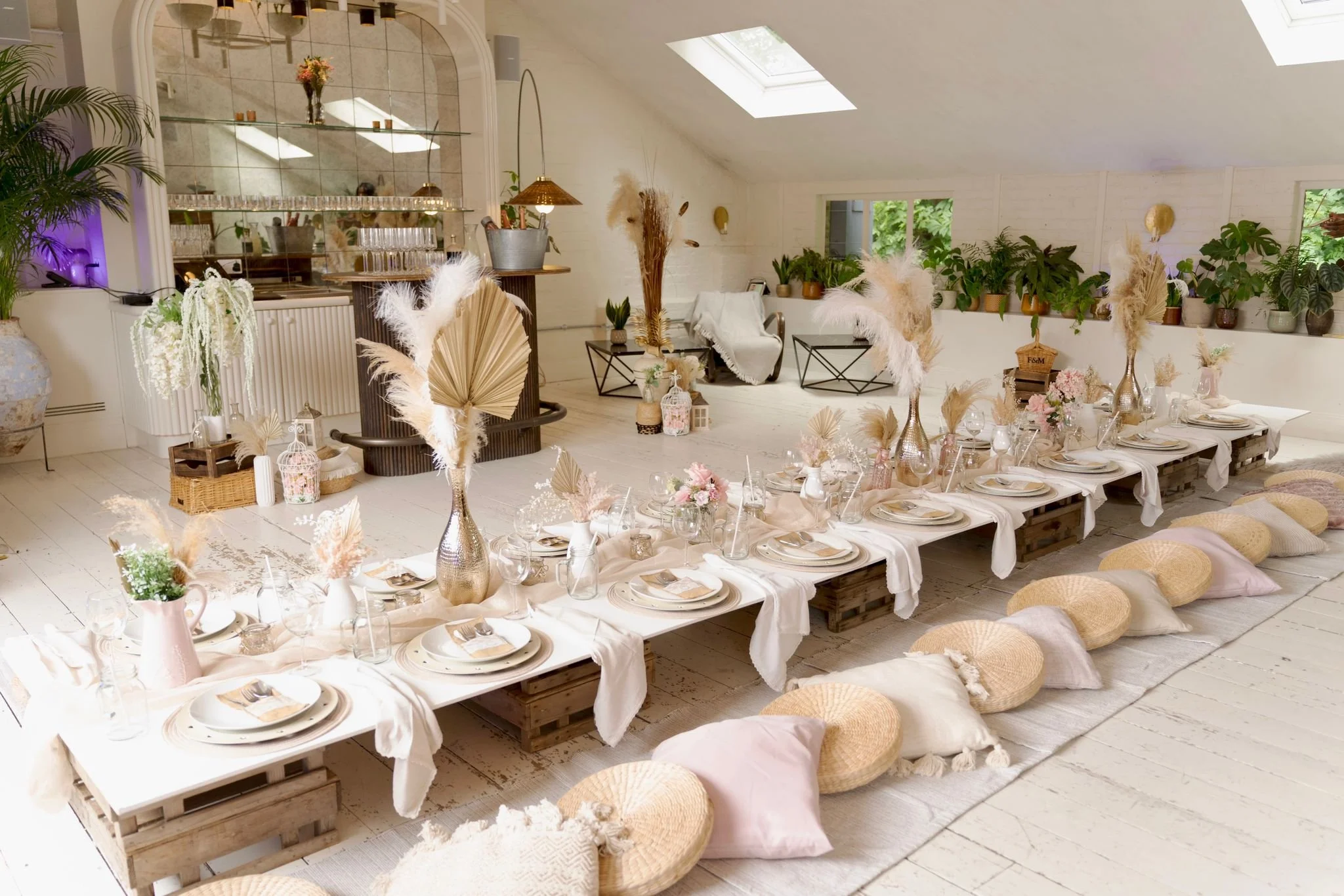 Private Dining space at Pyra London, with a long dining table set for a special occasion, featuring boho-chic vases with pampas grass, flowers, and soft cushions on the floor, with lush greenery along the windows and skylights overhead.